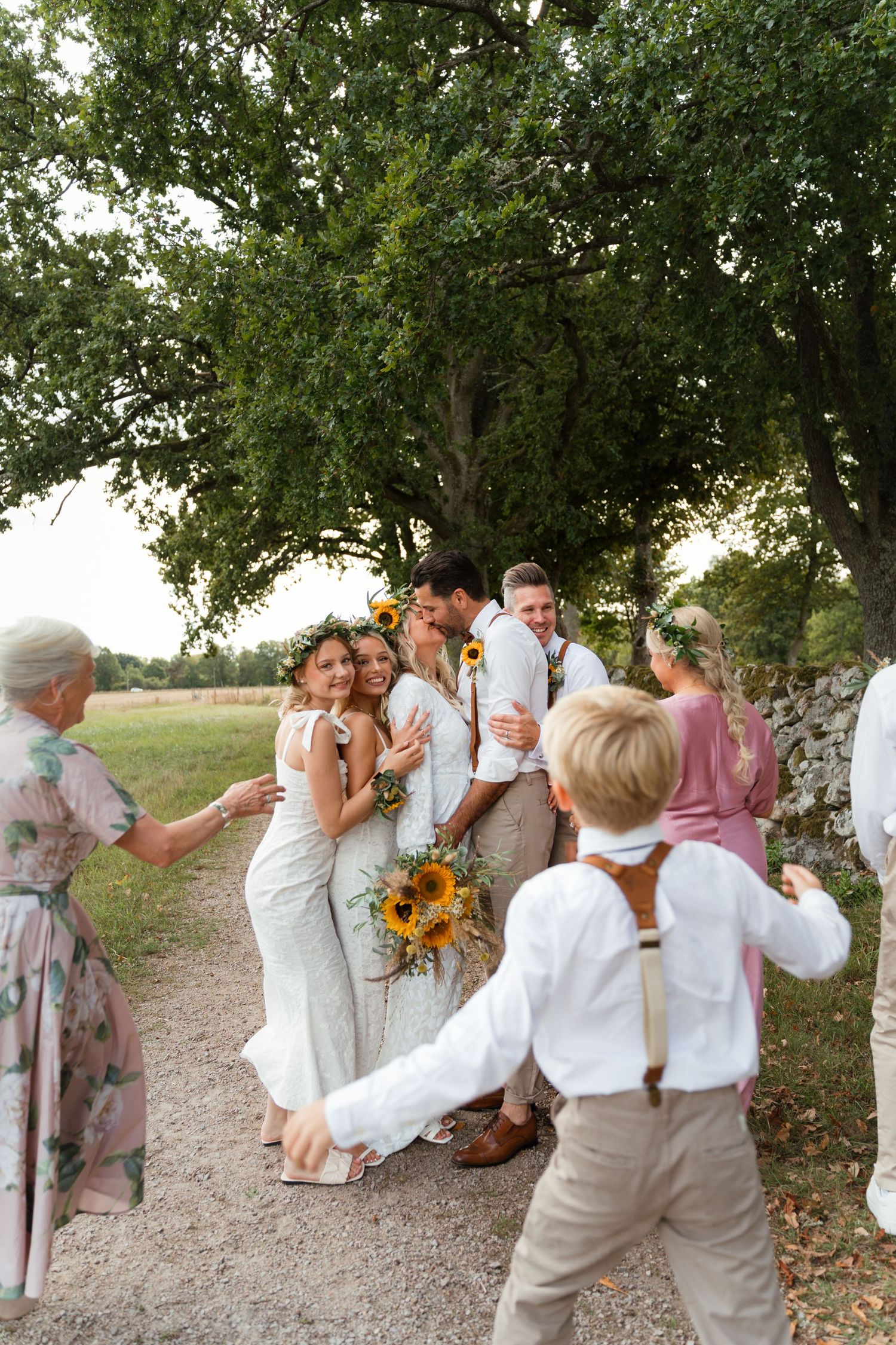 A joyful wedding party celebrates outdoors under large trees with sunflowers and rustic country decor.