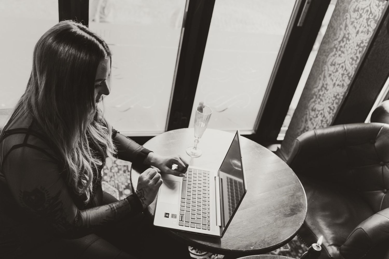 Woman working on laptop in black and white photography with soft natural lighting.