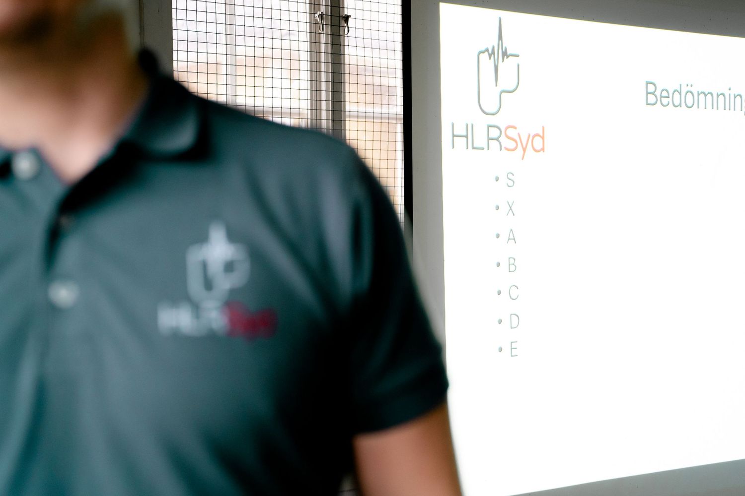 Professional instructor standing next to a presentation screen displaying a company logo.