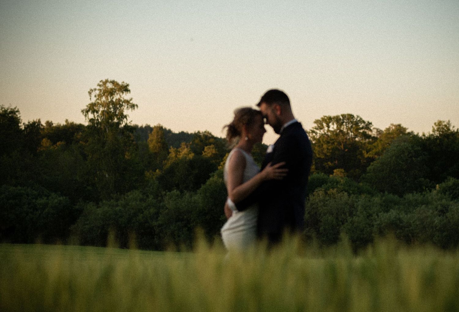 A silhouetted couple shares an intimate moment at dusk in a serene field.