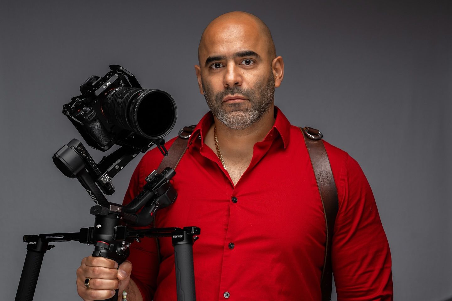 Professional photographer wearing red button down shirt holds professional camera rig against dark background.