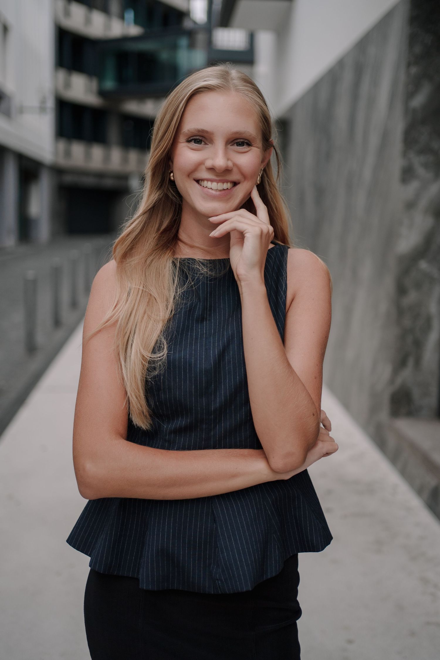 Smiling blonde woman in black sleeveless top posing outdoors near modern building.