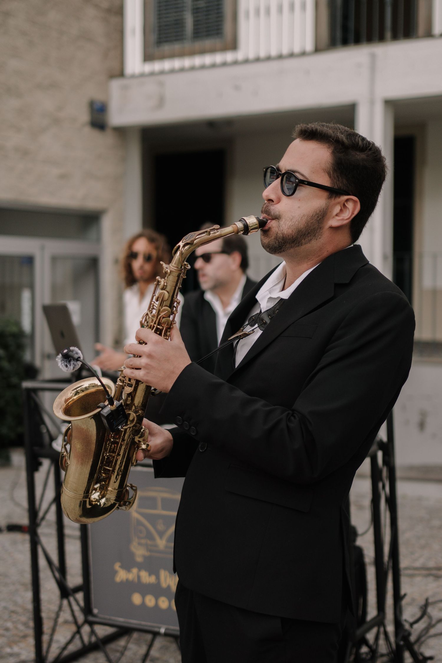 Musician in black suit playing saxophone outdoors at elegant event.