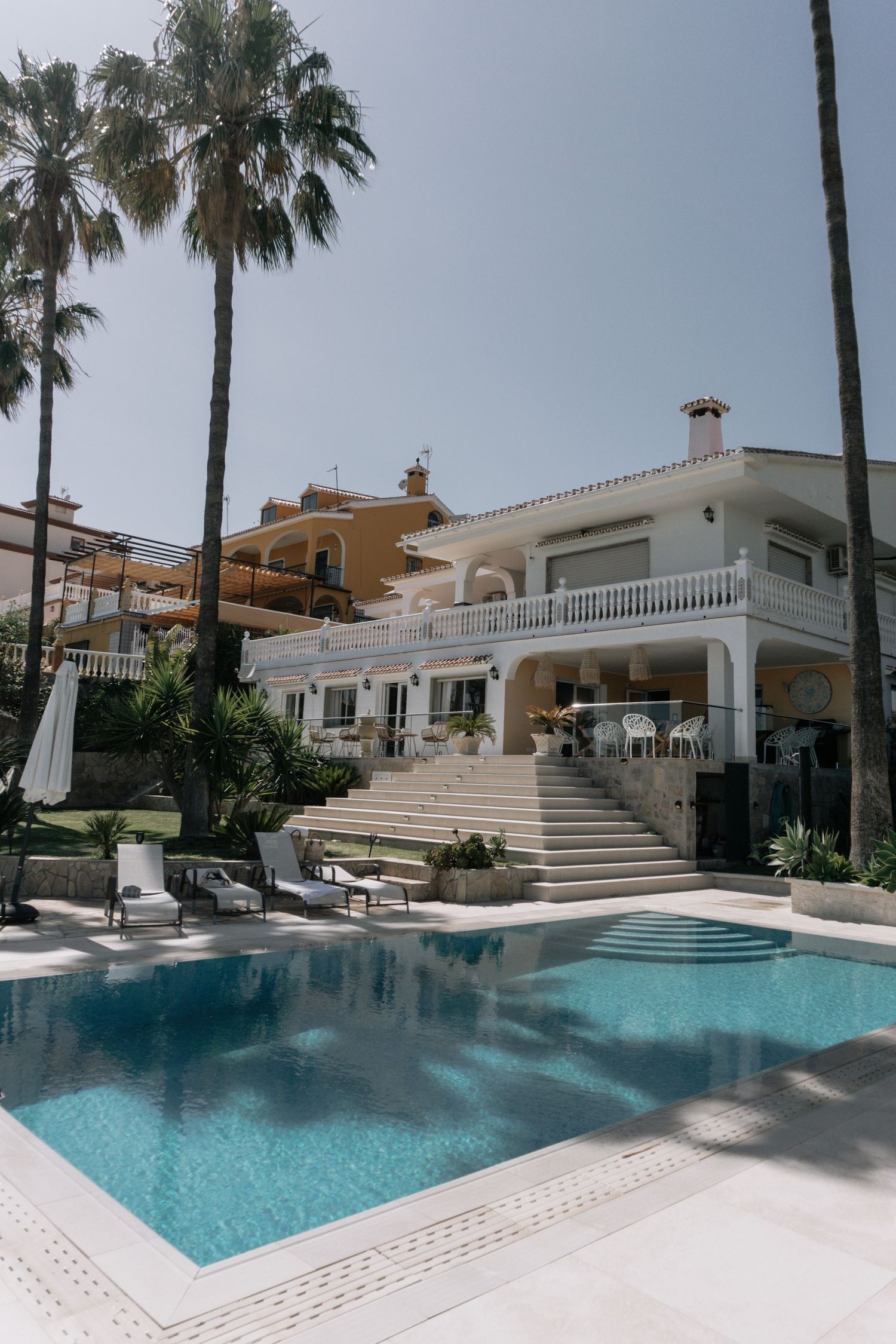 Luxury white villa with pool, palm trees, and balcony in sunny Mediterranean setting.