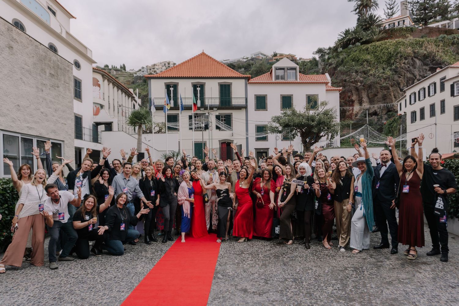 Large group of elegantly dressed people posing on a red carpet outdoors at a formal event in Madeira.