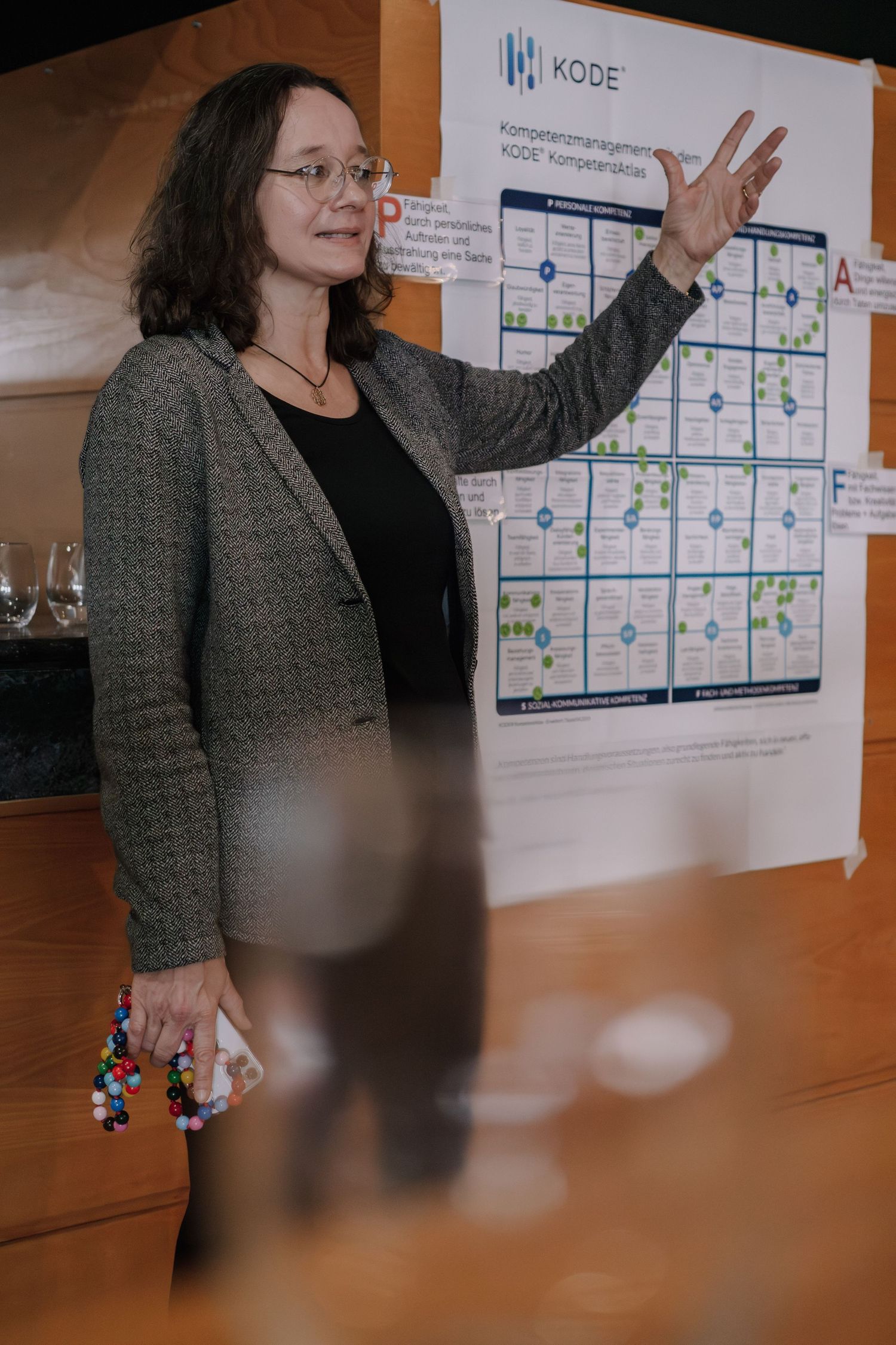 Woman presenting KODE competency management framework poster at a professional conference or workshop setting.