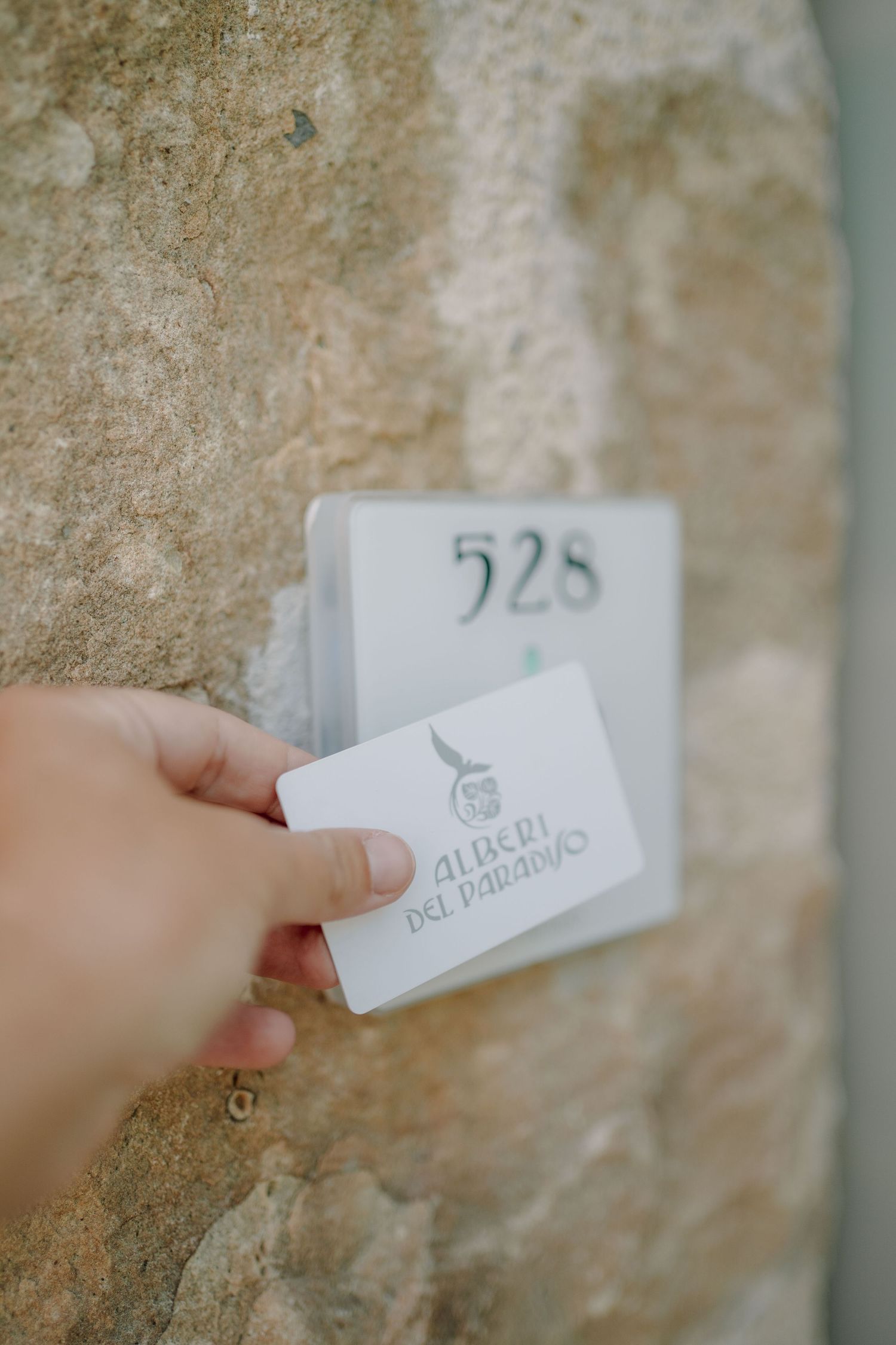 Hand holding an Alberi del Paradiso key card up to the door reader of room 528 on a rustic stone wall.