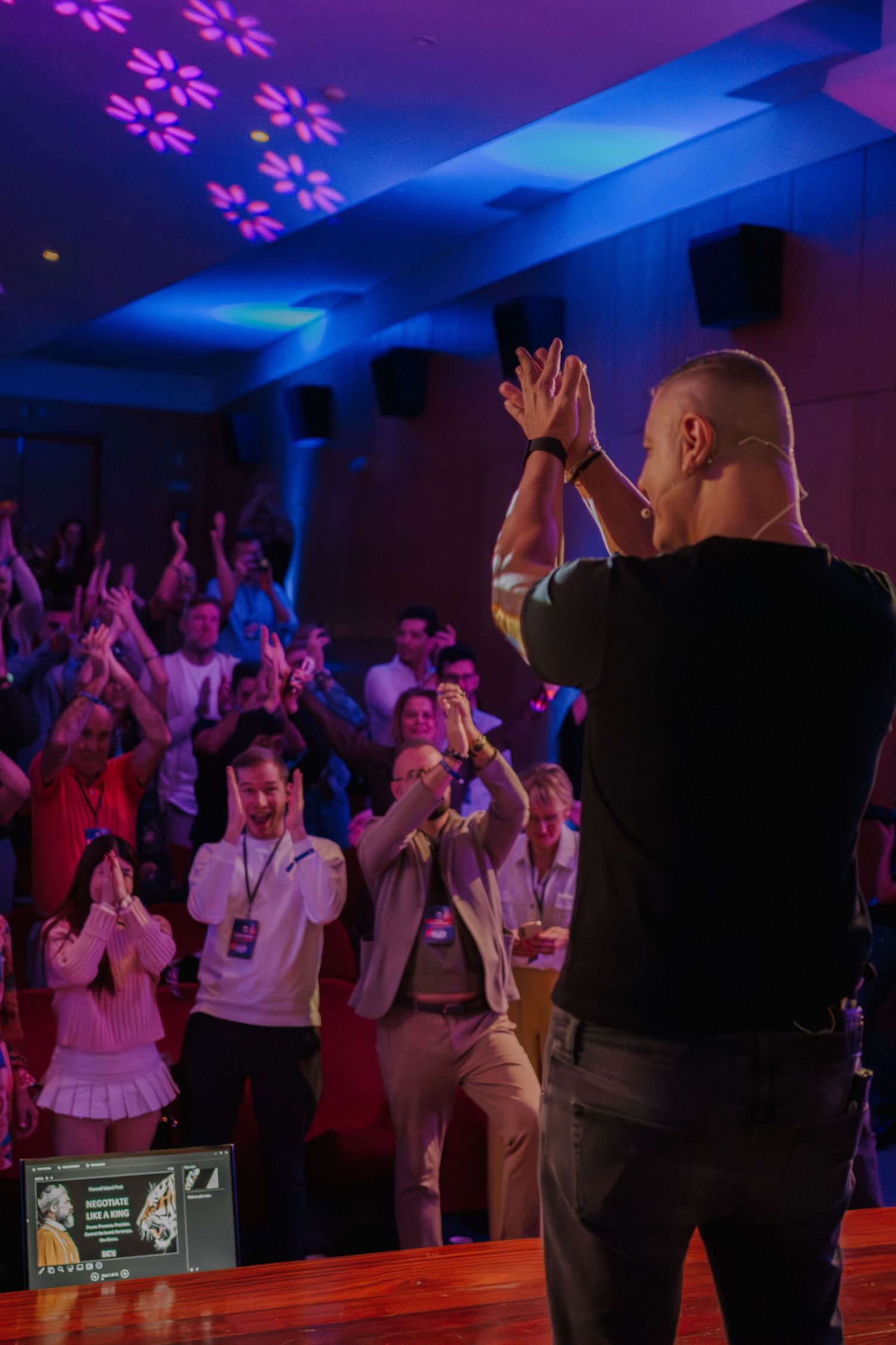 Performer on stage engaging enthusiastic crowd in blue-lit conference venue.