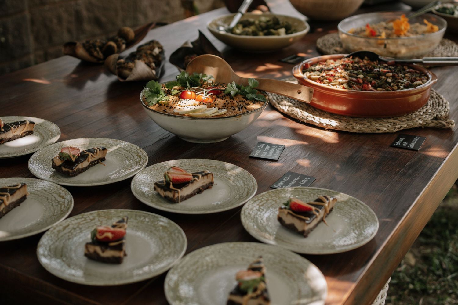 Rustic wooden table with plated appetizers and copper serving dishes filled with warm, hearty dishes at a dinner gathering.