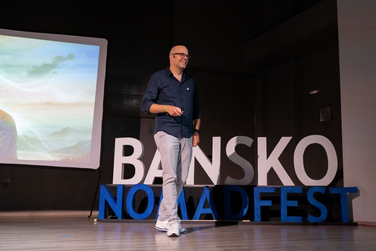 Speaker presenting on stage at Bansko Nomad Fest conference with projection screen in background.