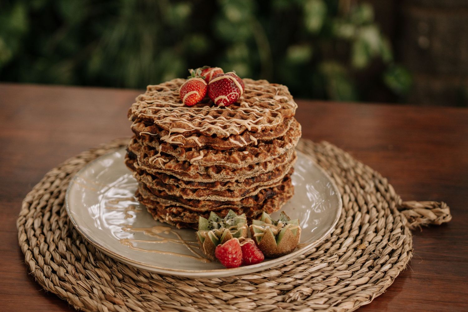 Stack of chocolate waffles topped with fresh strawberries on ceramic plate with woven mat.