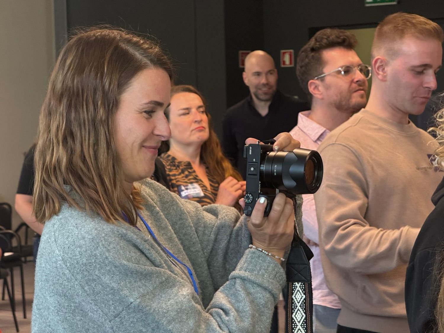 Woman holding a camera at an indoor photography event with a group of people standing in the background.
