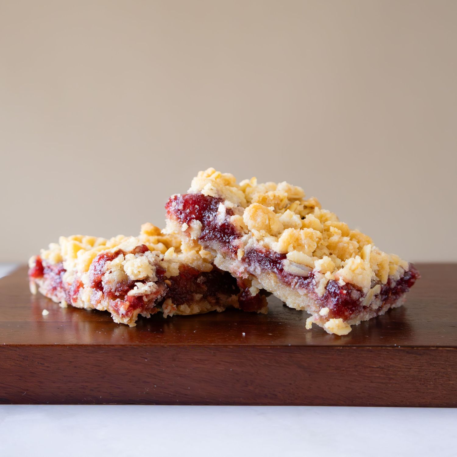 Raspberry crumble bars with buttery streusel topping stacked on a wooden cutting board.