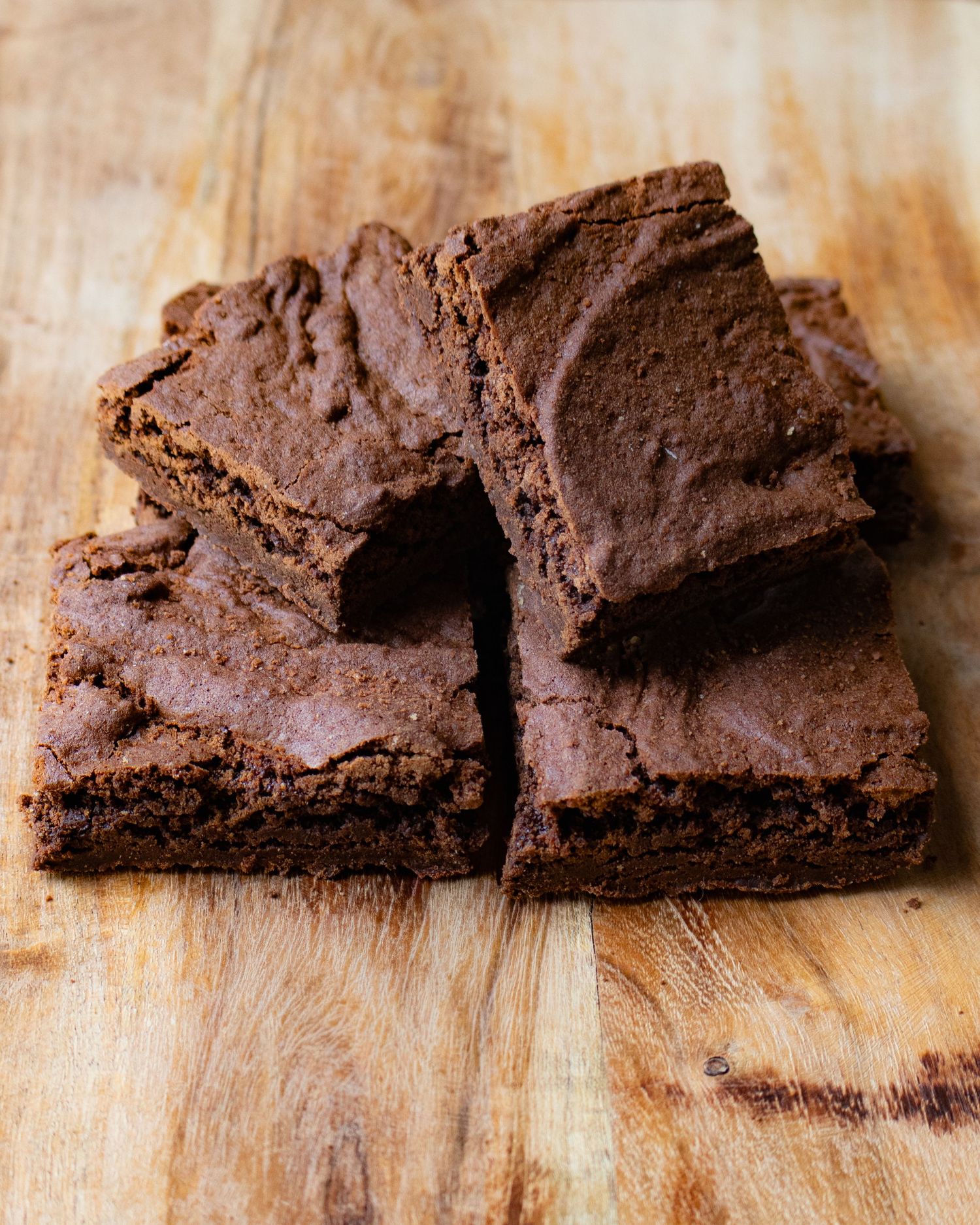 Stack of fudgy chocolate brownies on a wooden cutting board, rich and dense with a crackly top.