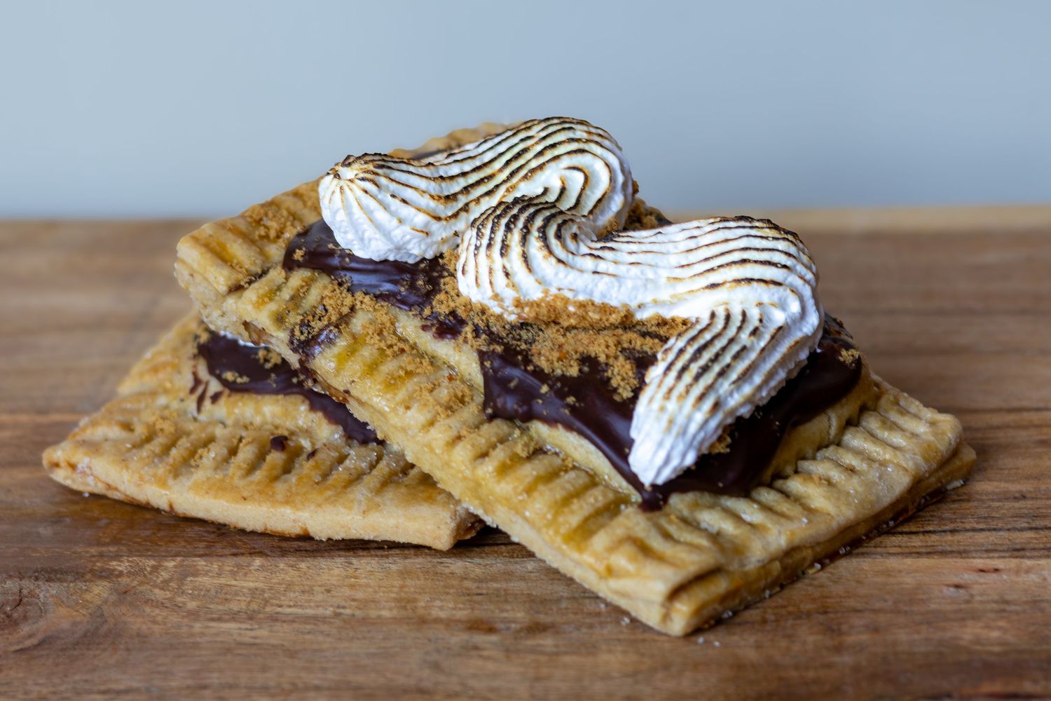 S'mores pop tart with toasted meringue, chocolate filling, and graham cracker crust on a wooden surface.