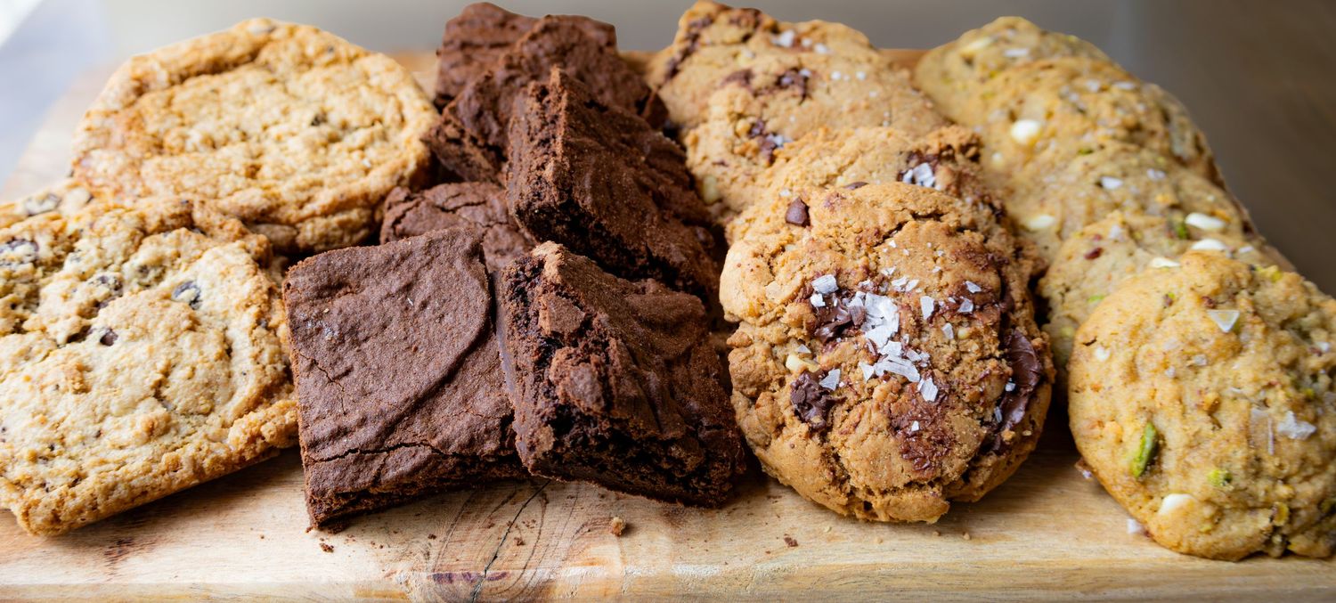 Assorted homemade cookies and fudgy chocolate brownies displayed on a wooden cutting board.