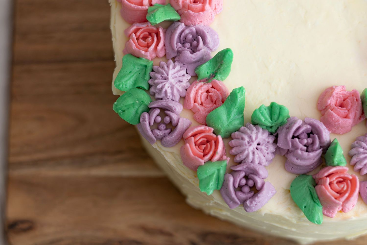 Close-up of a white frosted cake decorated with pink and purple buttercream roses and green leaves.