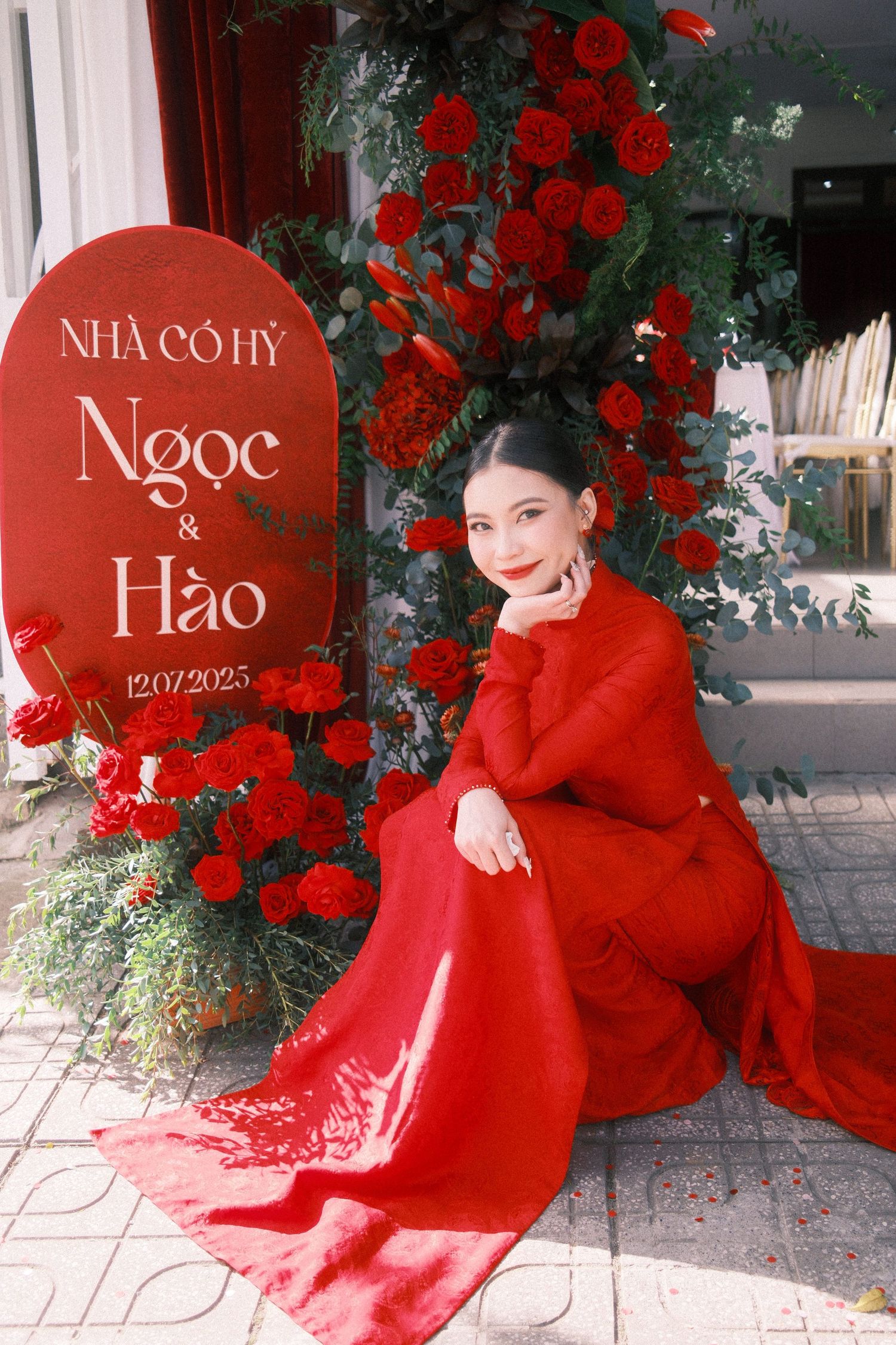 Woman in red dress poses by Vietnamese wedding sign with roses for Ngoc and Hao, dated 12/07/2025.