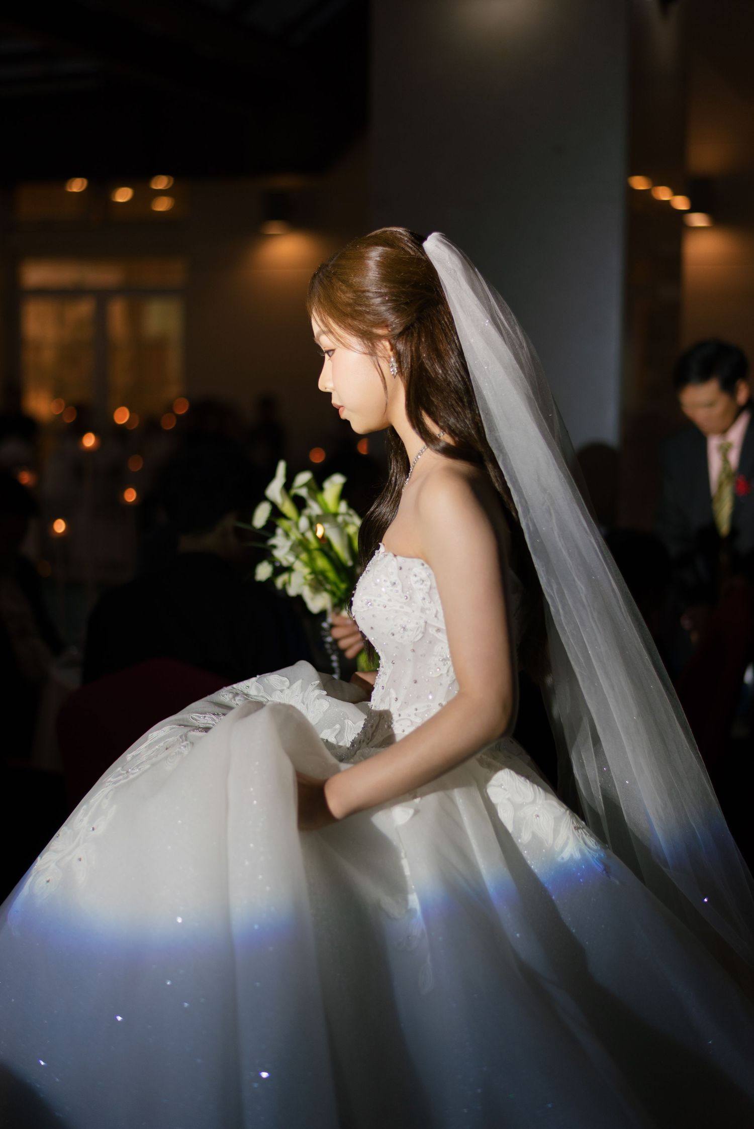 Bride in a stunning white ball gown with veil holding a bouquet of white flowers during a wedding ceremony.