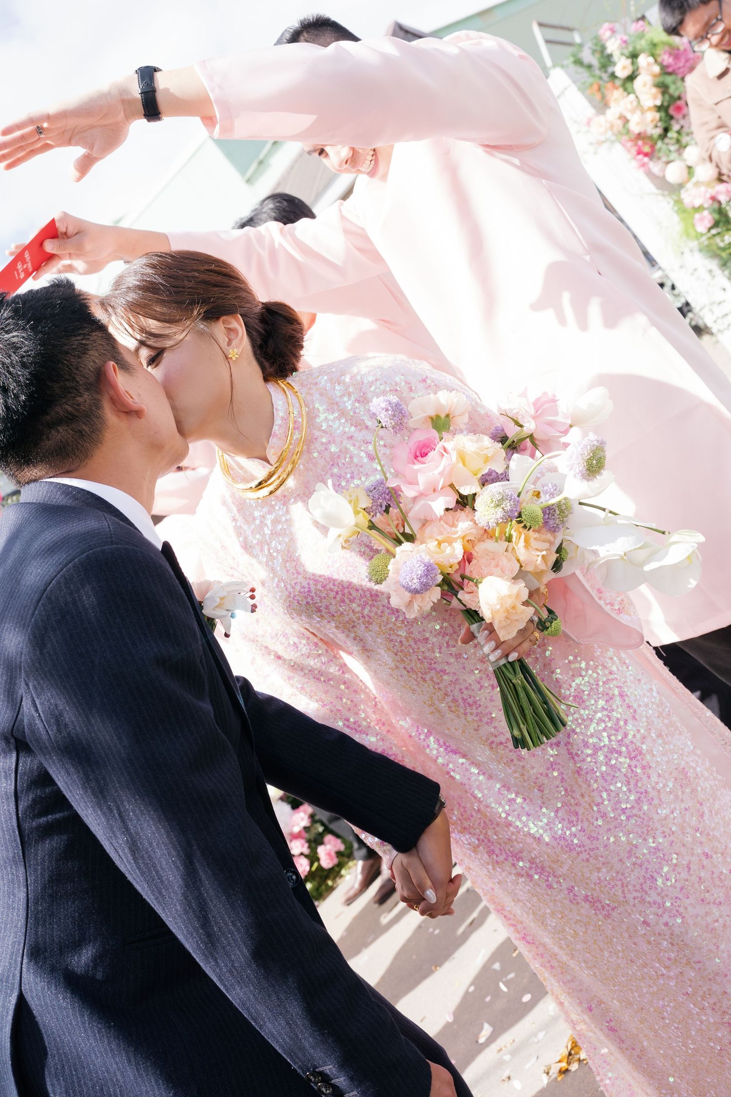 Bride and groom share a kiss as bride holds pastel bouquet at outdoor Vietnamese wedding ceremony.