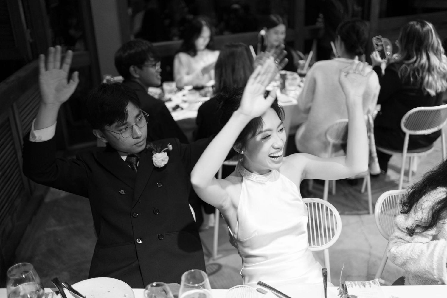 Bride and groom celebrate joyfully at wedding reception dinner in black and white photo.