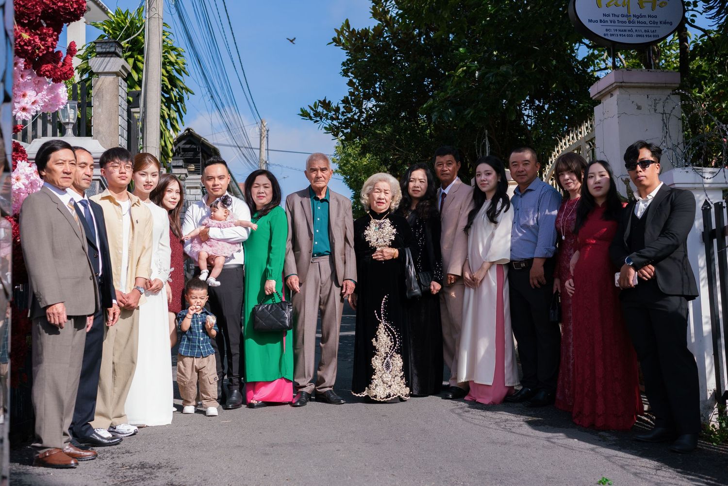 Large Vietnamese family group posing together outdoors at a gate during a wedding celebration.