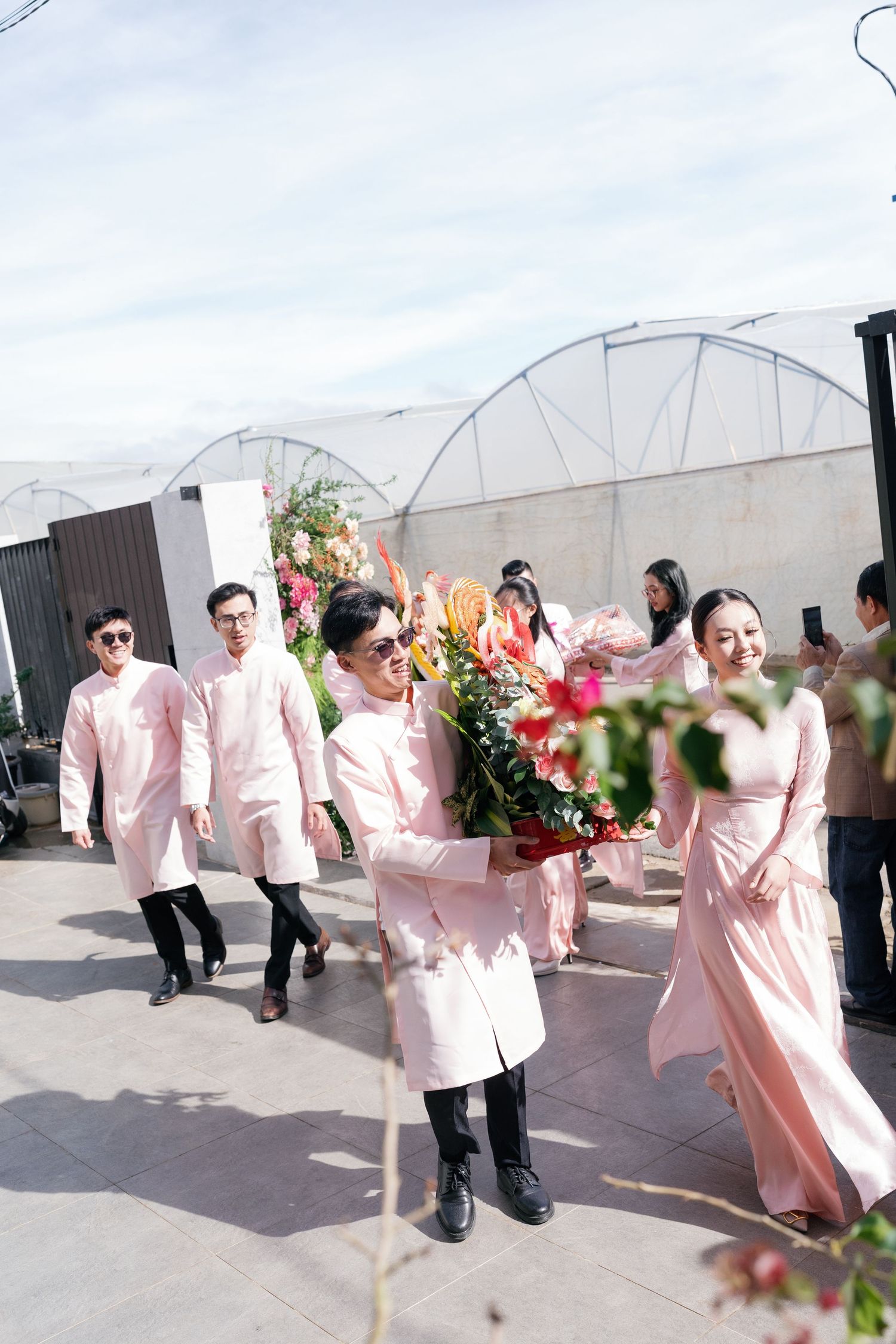 Groomsmen in pink ao dai carrying floral arrangements at a Vietnamese traditional wedding.