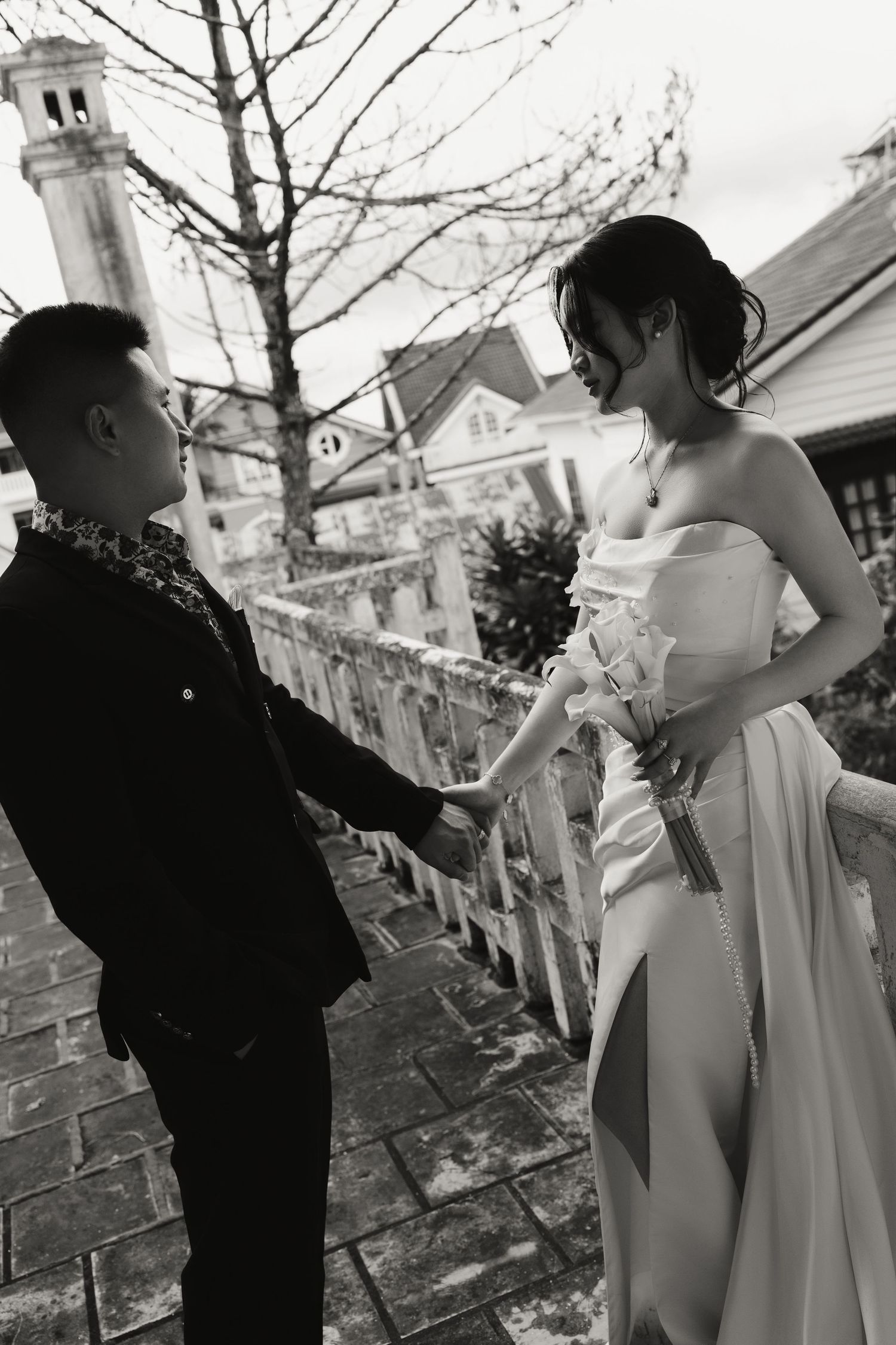 Black and white image of bride and groom facing each other on stone steps near charming buildings.