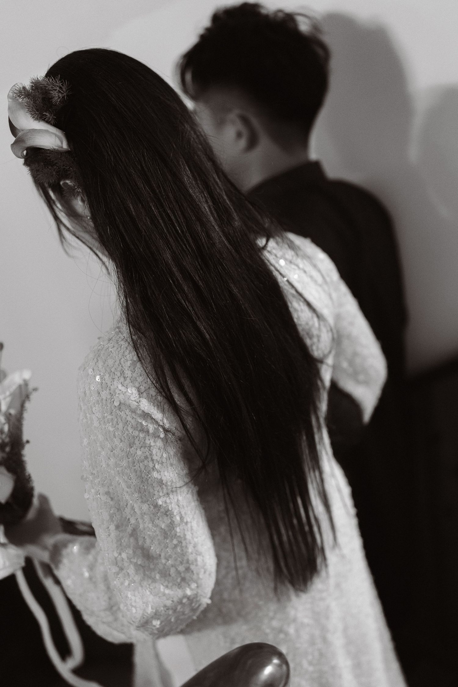 Black and white photo of a bride in white dress with long dark hair facing away from groom at wedding.