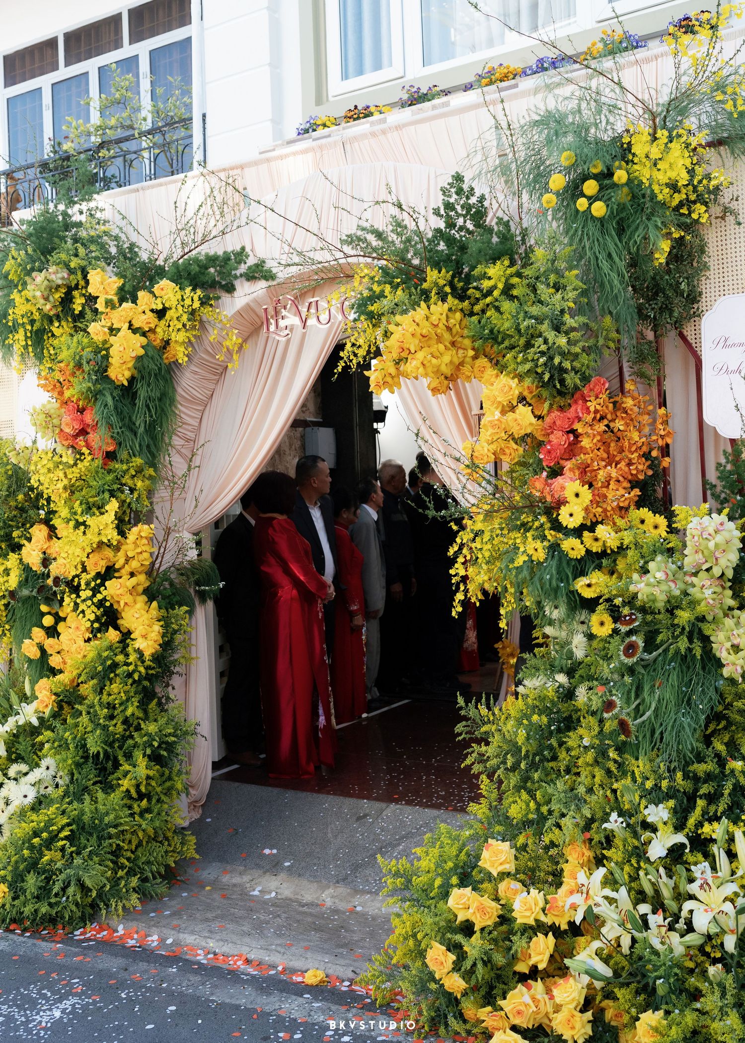 Floral arch entrance adorned with vibrant yellow, orange, and green flowers framing a draped doorway for a festive event.