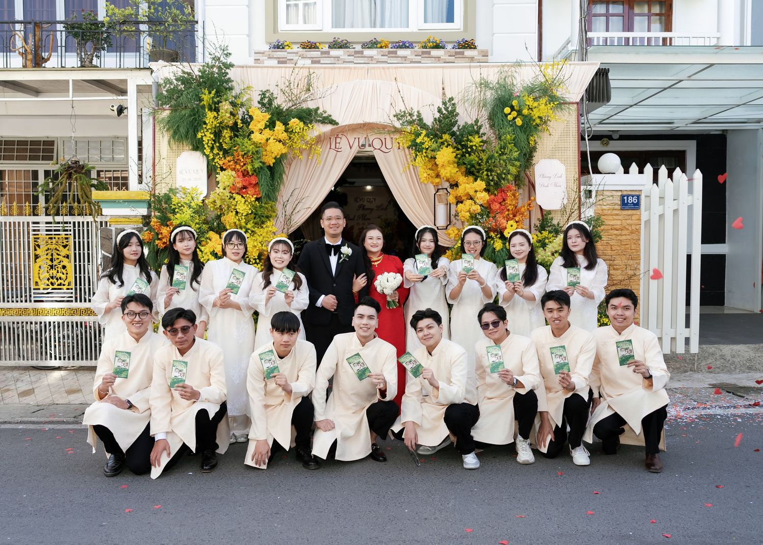 Vietnamese wedding party poses in traditional ao dai attire before a floral decorated entrance gate.