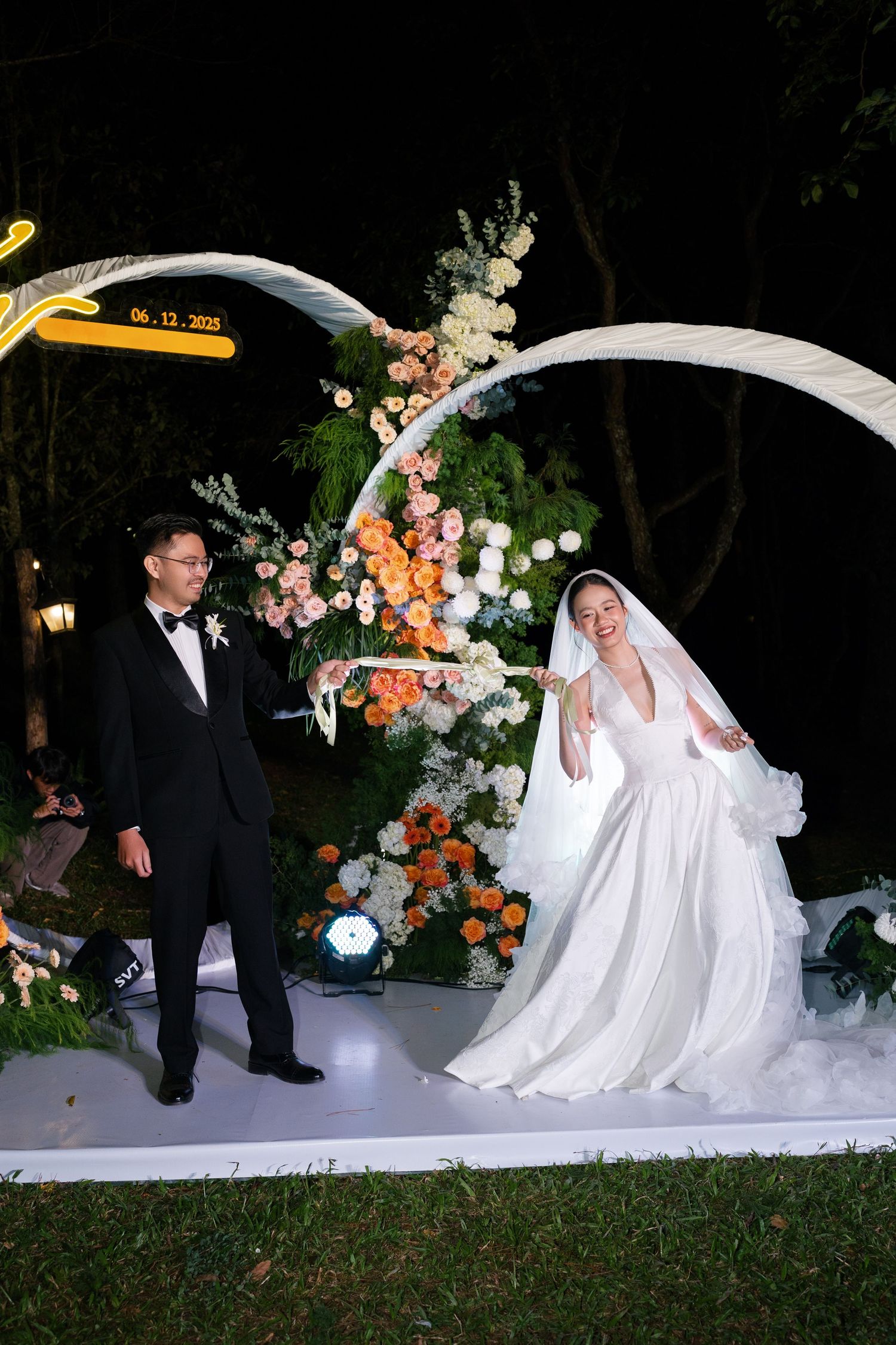Bride and groom celebrate at outdoor evening wedding ceremony with floral arch and colorful blooms on June 12, 2023.