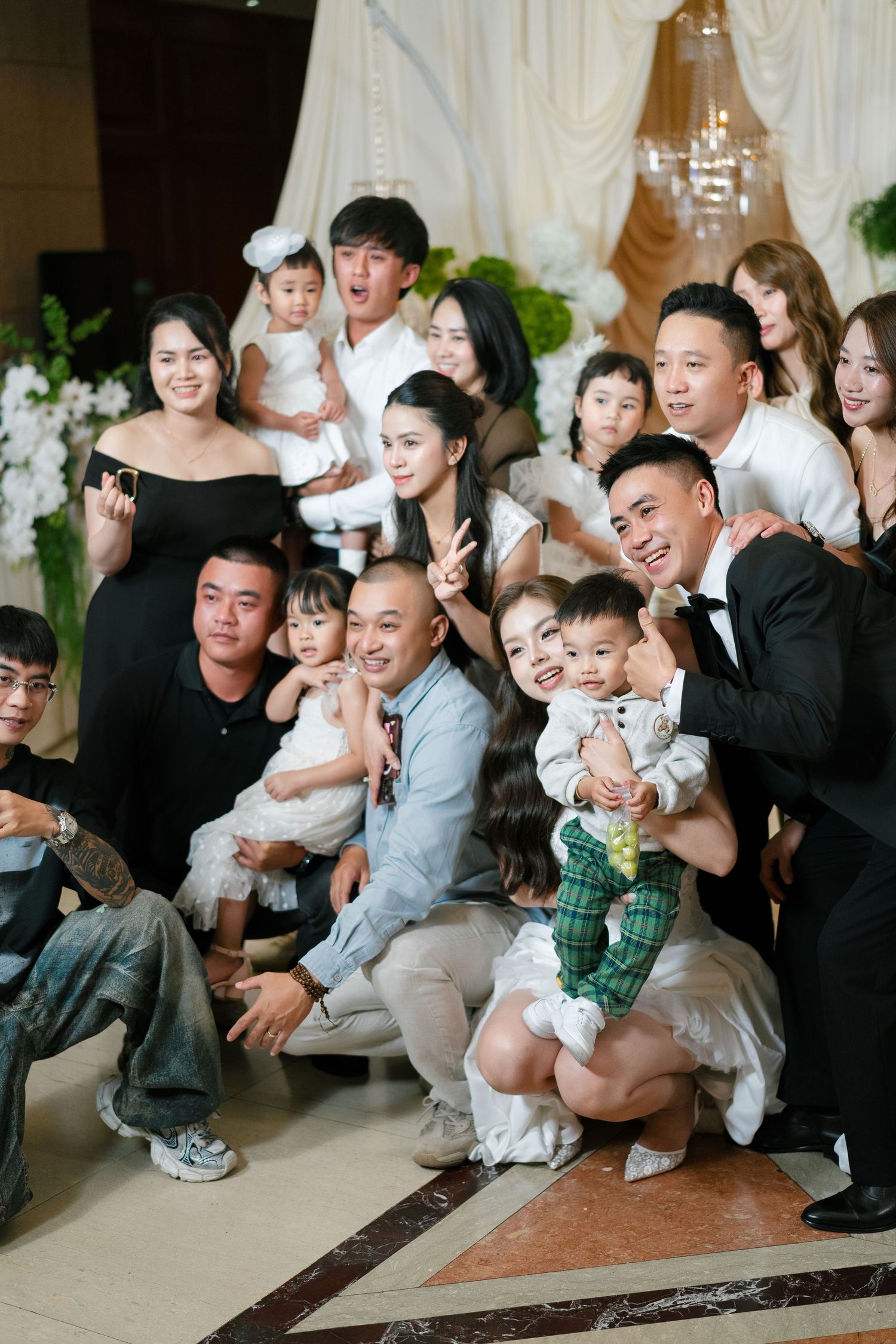 Large family group photo at a wedding celebration, with adults and children posing together in elegant attire.