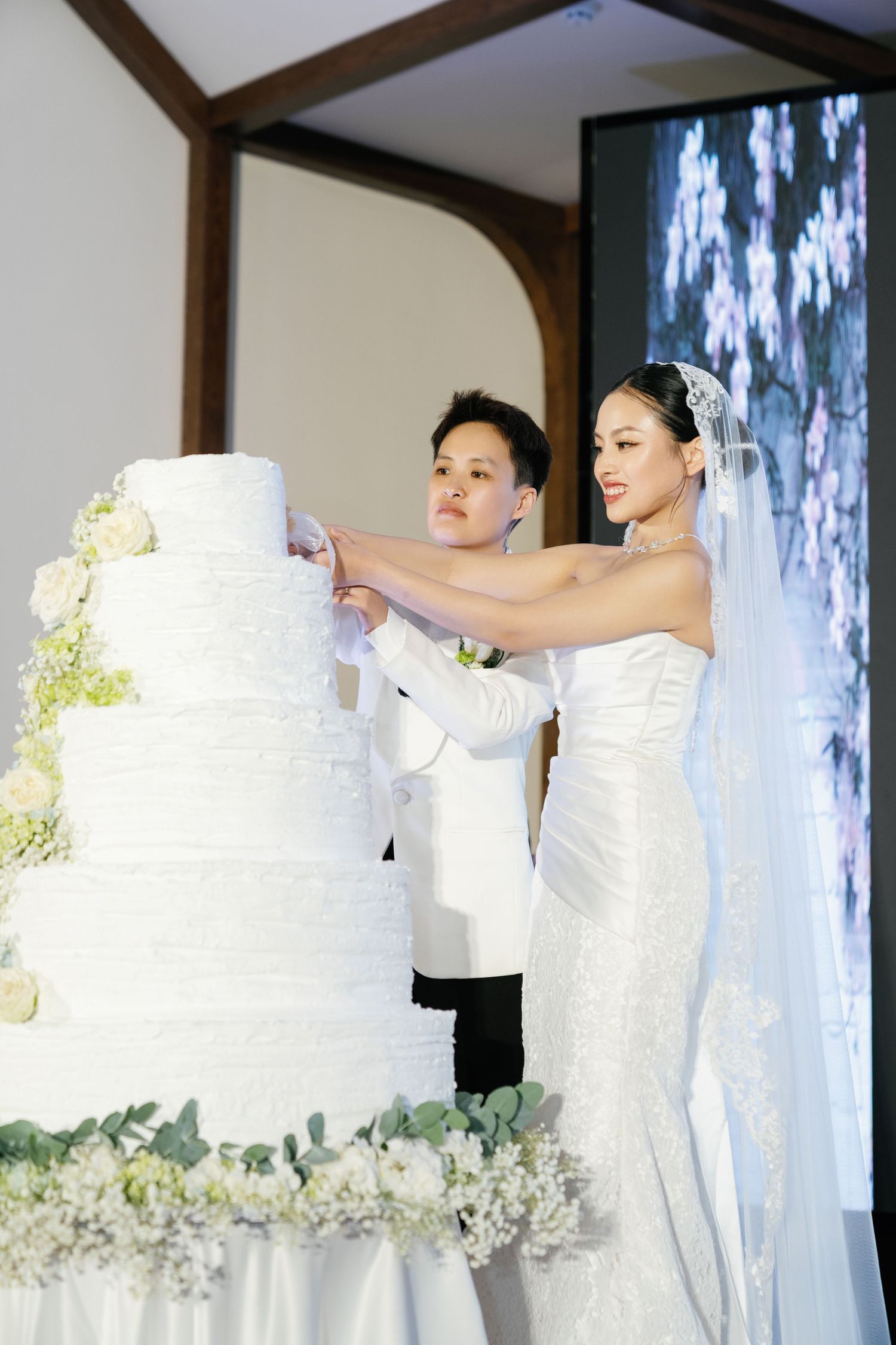 Bride and groom cutting elegant five-tier white wedding cake together at reception celebration.