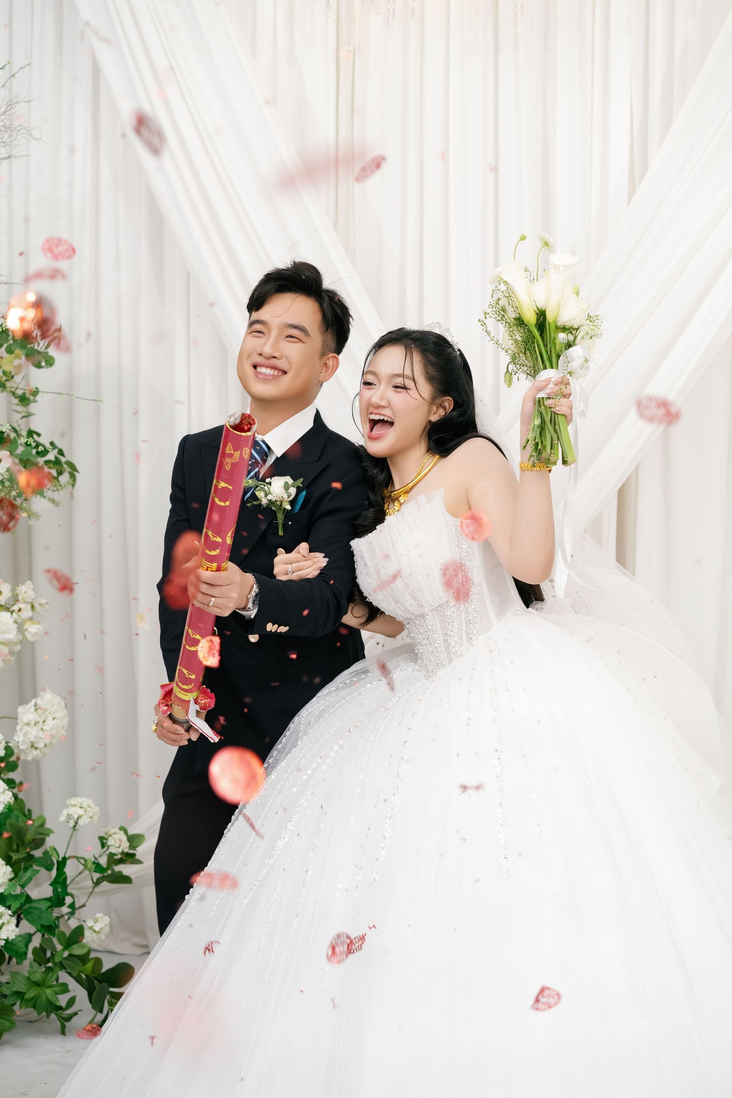 Joyful bride and groom celebrate with confetti cannon at elegant white wedding venue.