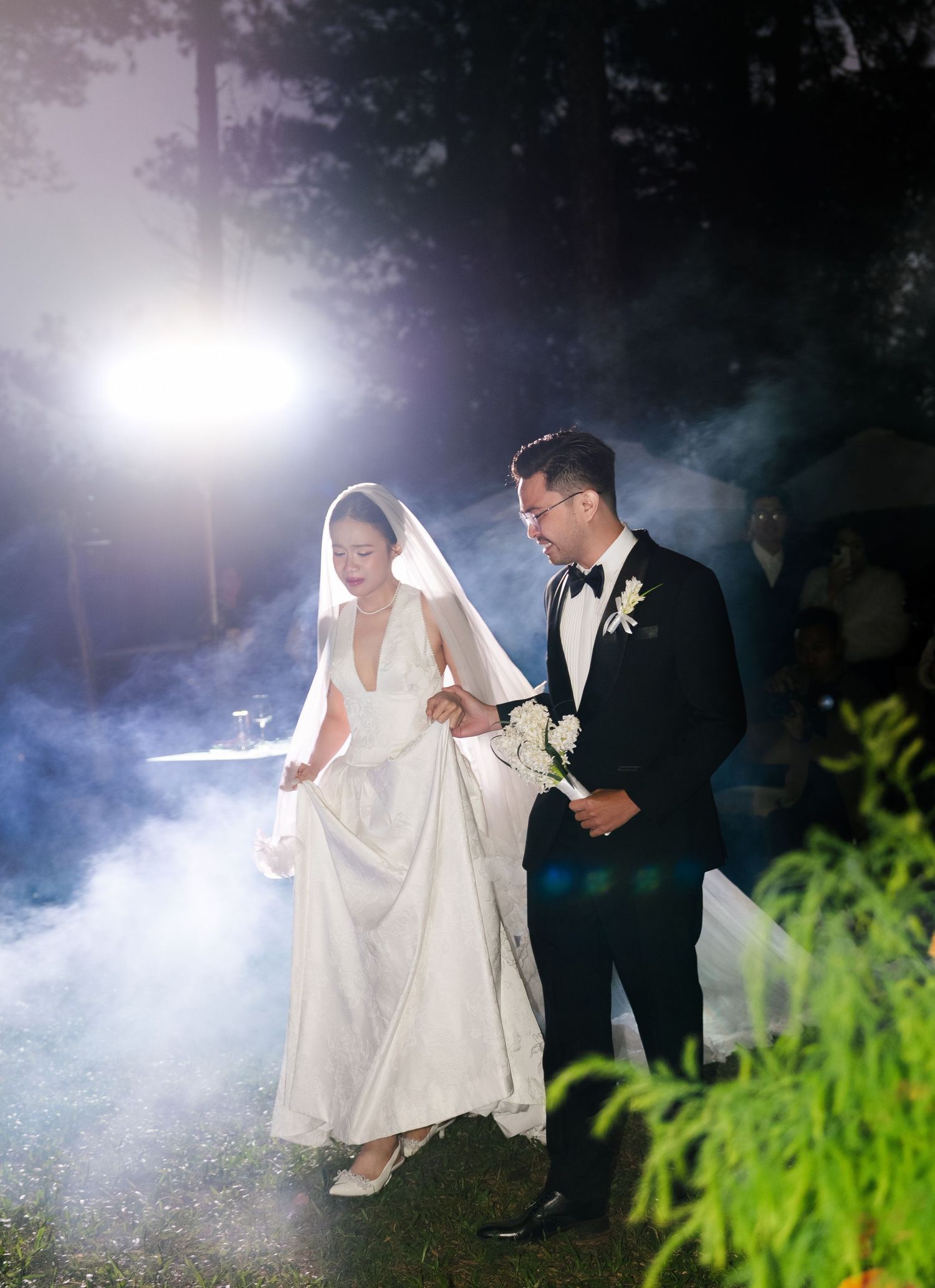 Bride and groom making grand entrance through dramatic smoke and bright lights at outdoor night wedding.
