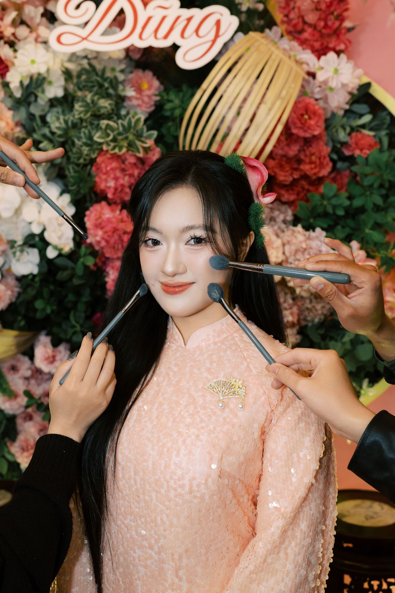 Young Vietnamese bride in pink ao dai gets makeup applied by multiple artists before her wedding ceremony.