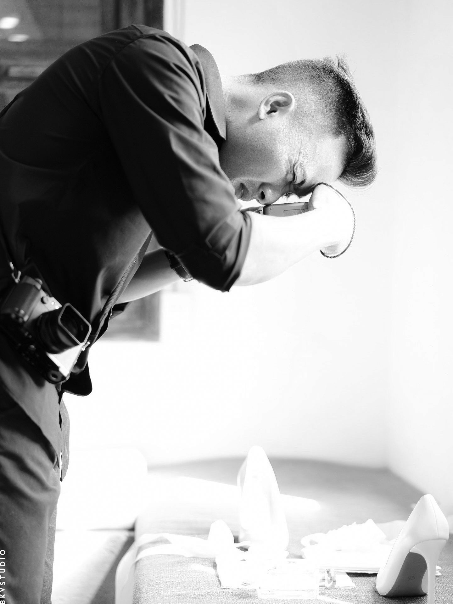 Black and white portrait of a groom in suit leaning over a table with wedding accessories.