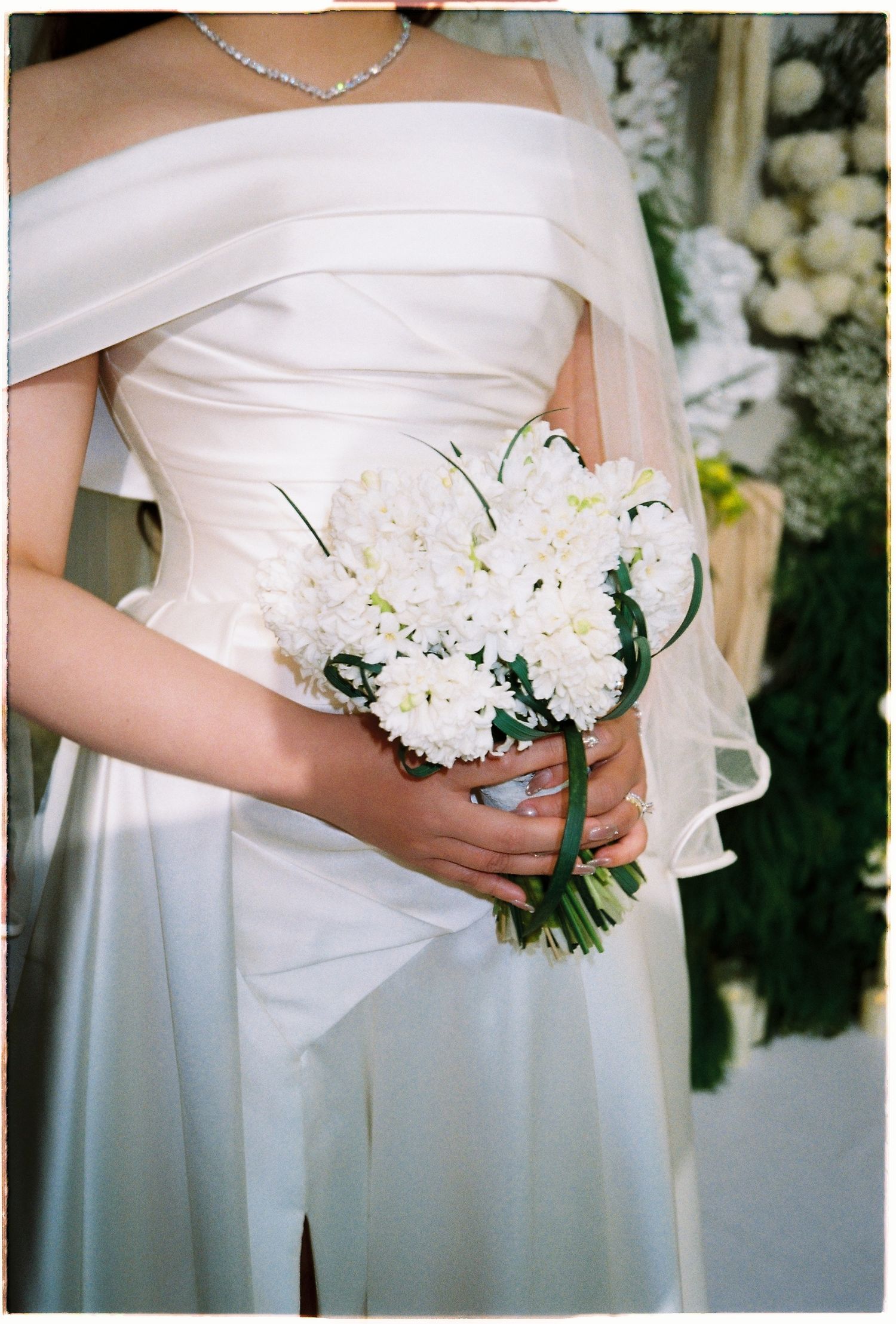 Close-up of bride in white strapless gown holding a bouquet of white chrysanthemums and lilies.