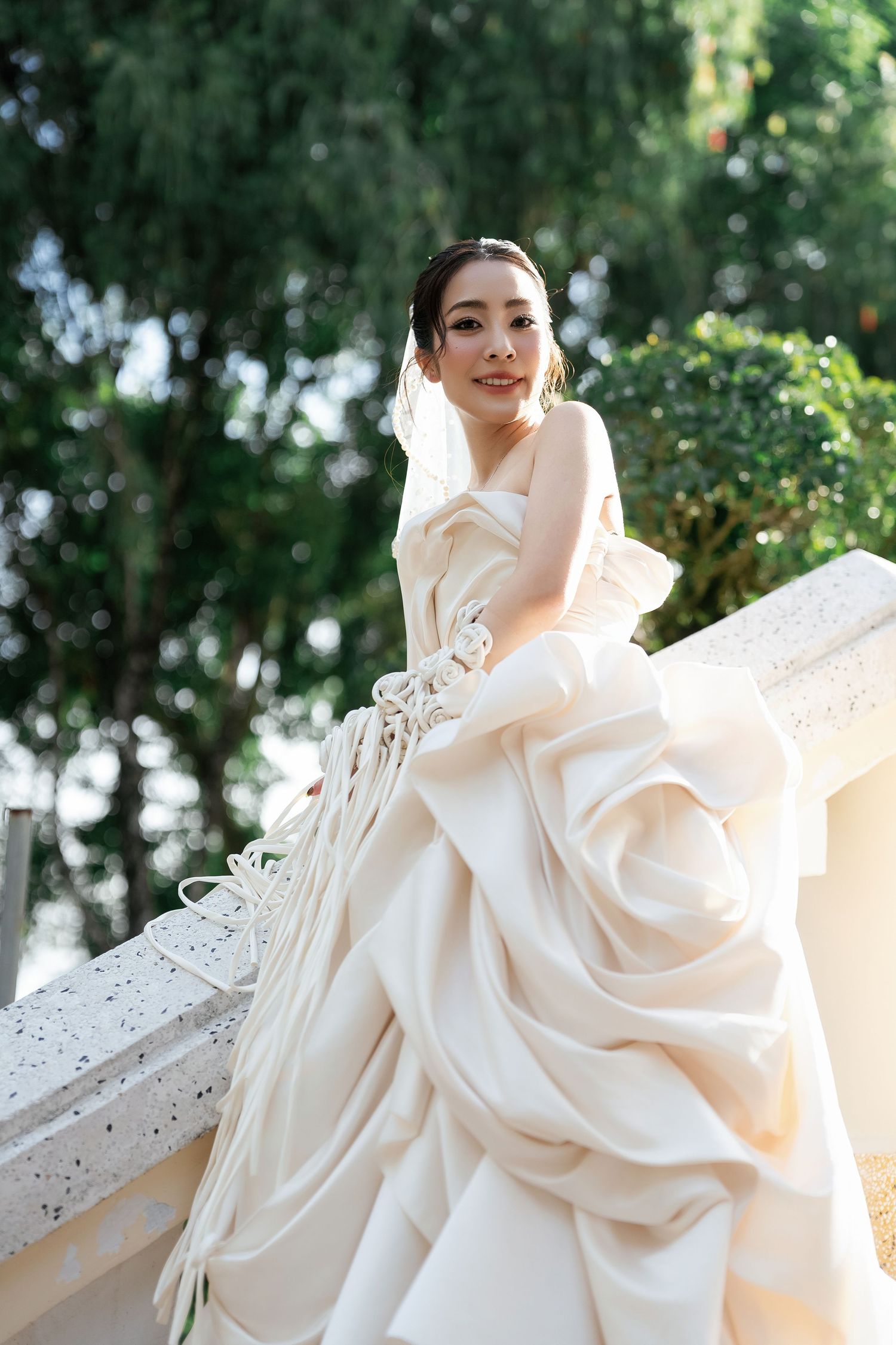 Elegant bride in voluminous ivory wedding dress posing on outdoor terrace.