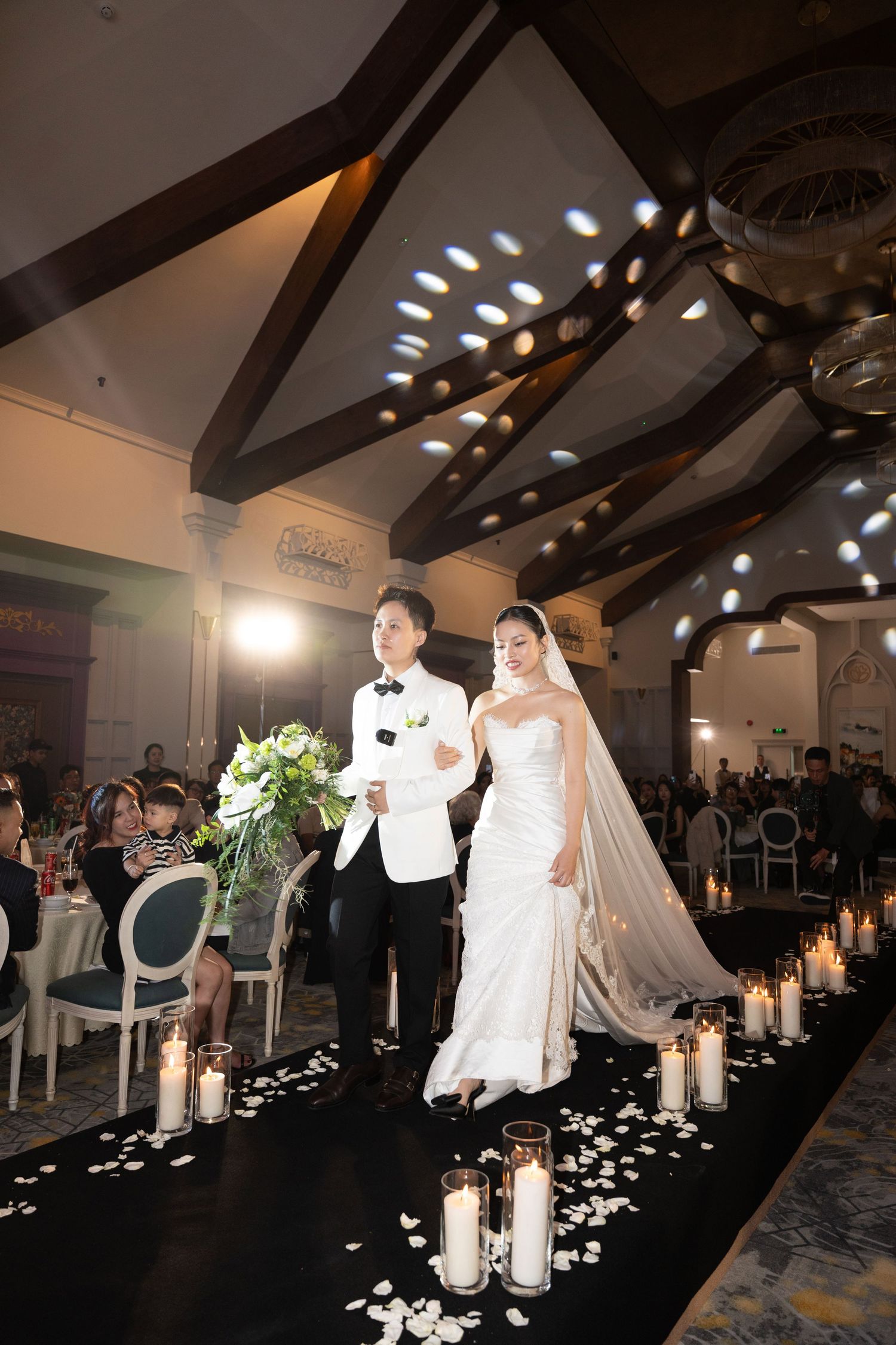 Bride and groom walking down candlelit aisle in elegant wedding reception hall.