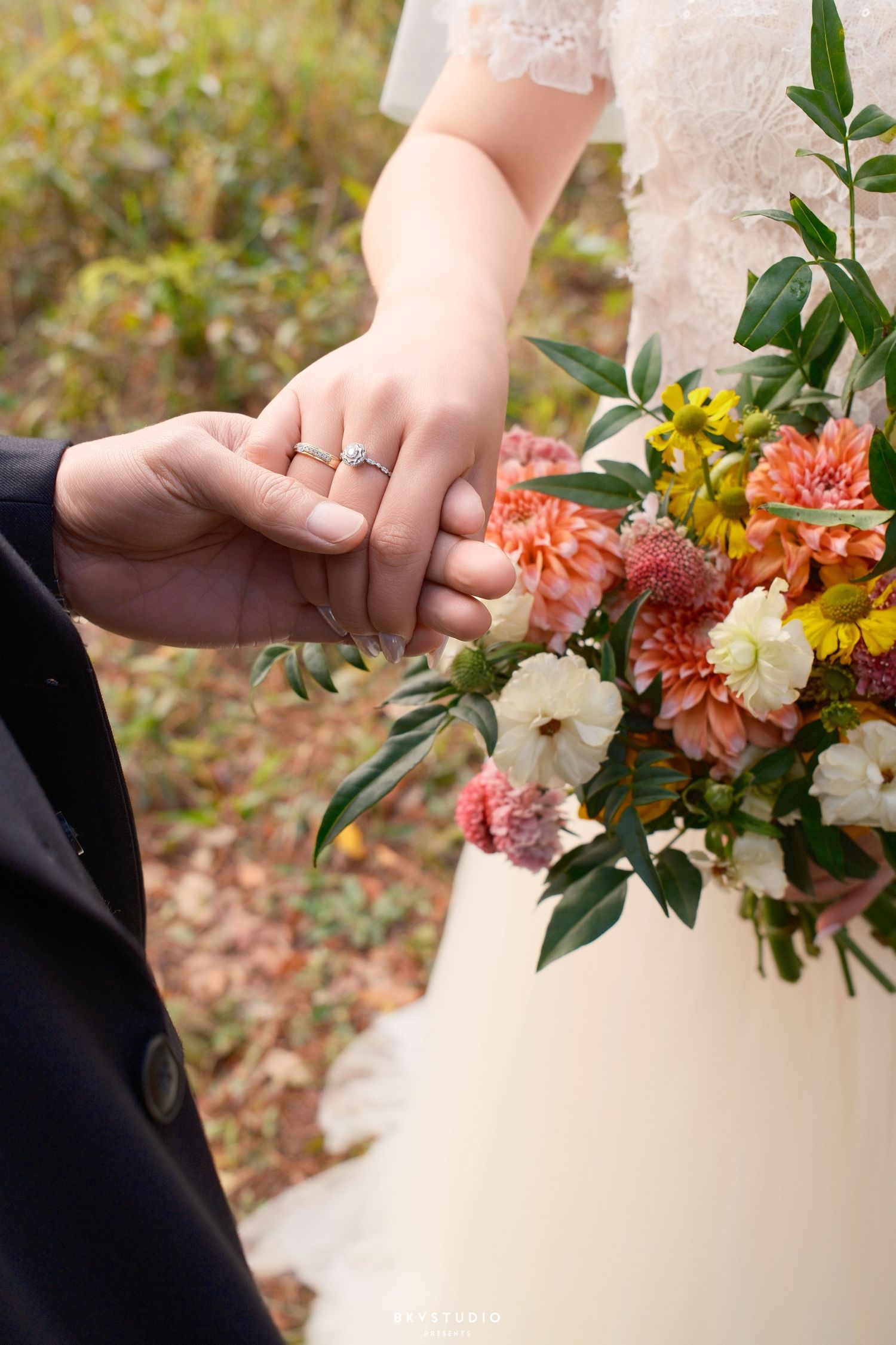 Close-up of newlyweds holding hands with wedding ring visible beside a vibrant bridal bouquet.