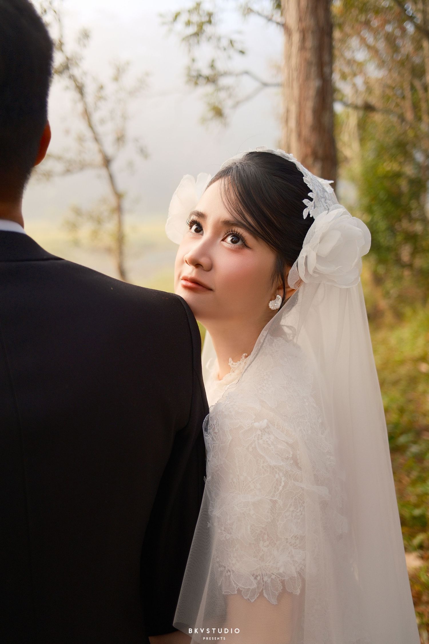 Bride in white lace gown and veil gazes up at groom during romantic outdoor wedding photo session.