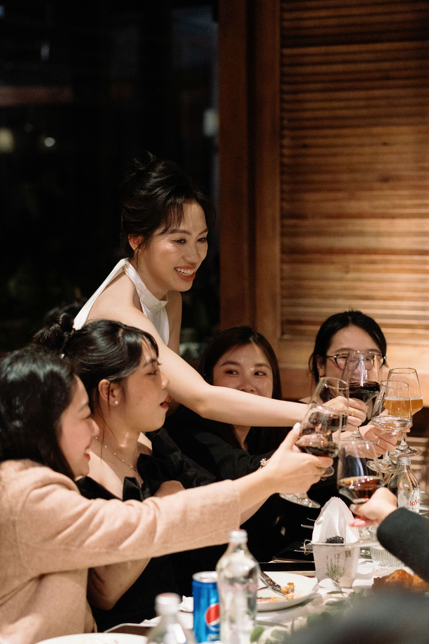 Bride toasting with wine glasses alongside smiling female guests at a wedding reception dinner.