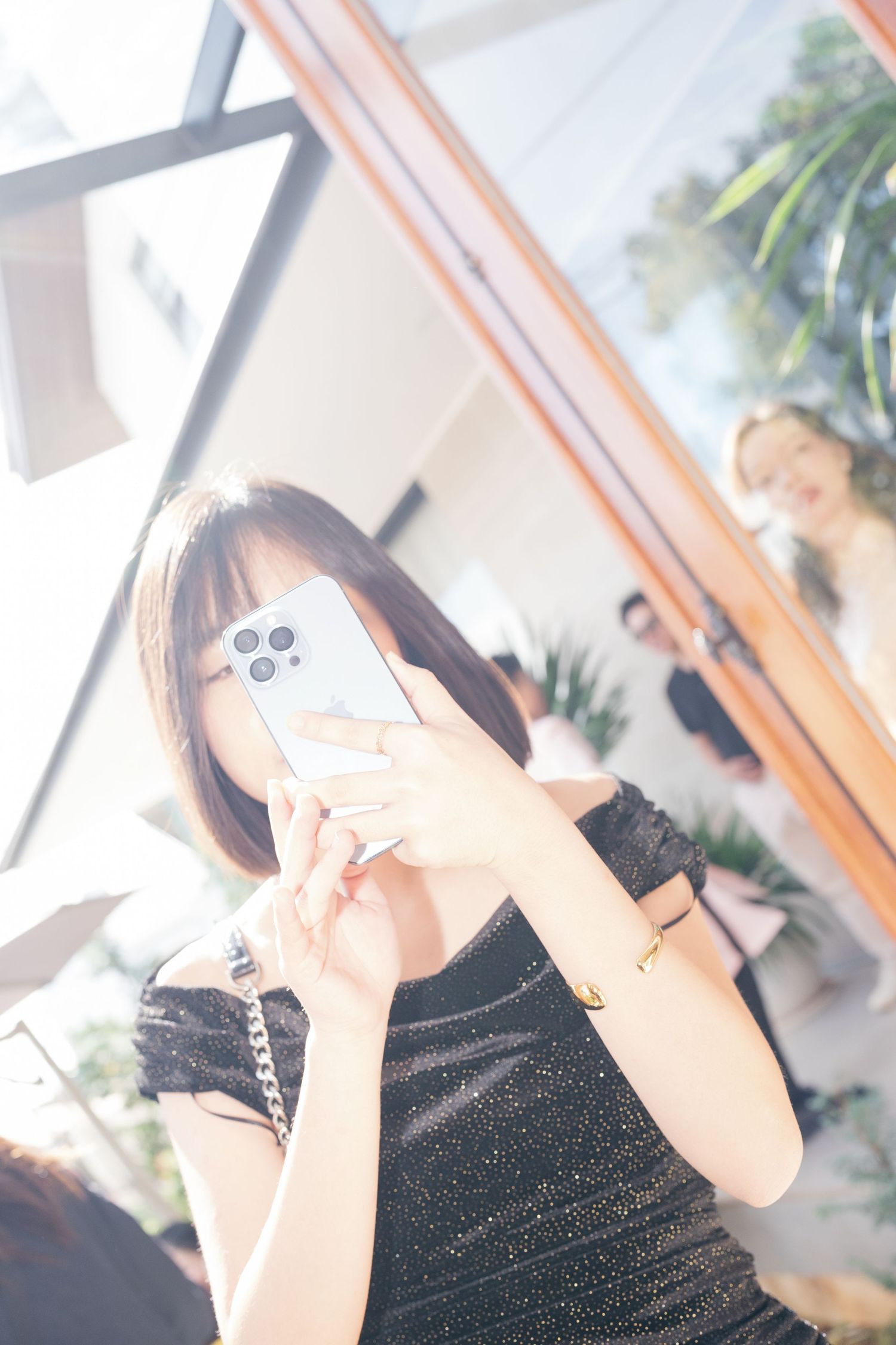 Young woman taking a mirror selfie with a white iPhone in a bright room.