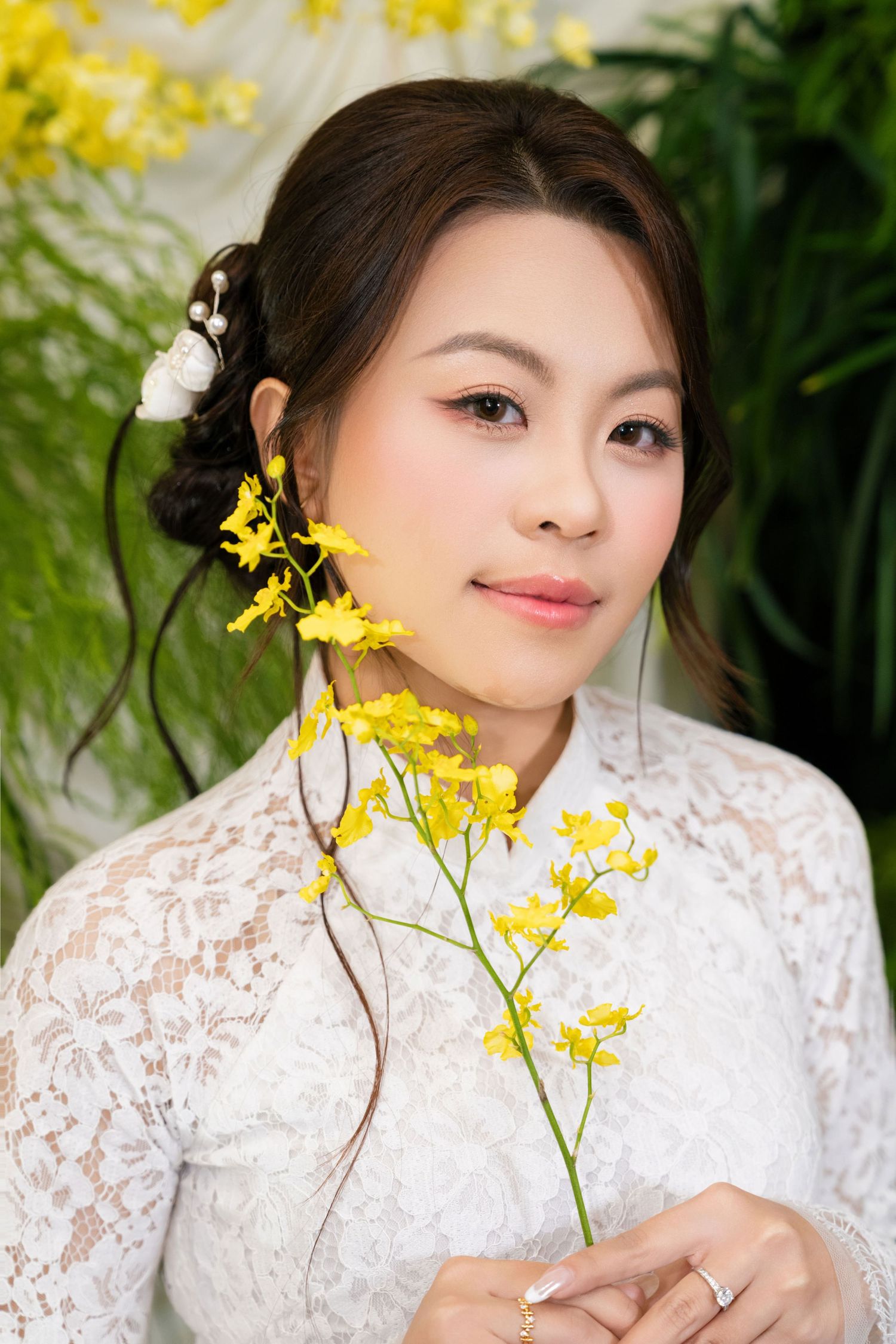 Asian bride in white lace dress holding yellow orchid flowers with elegant updo hairstyle.