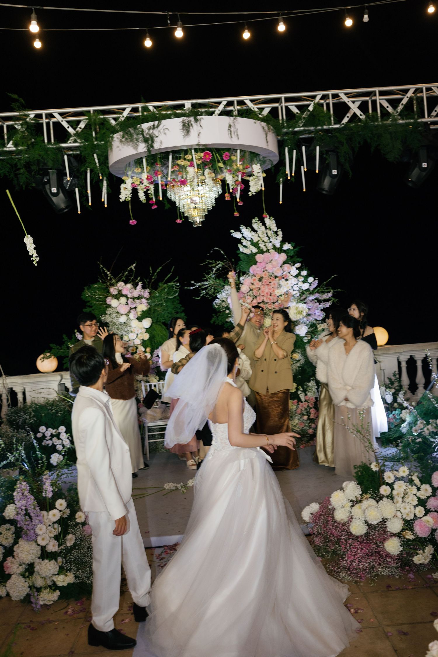 Bride and groom celebrate at an elegant outdoor night wedding ceremony adorned with floral arrangements and string lights.