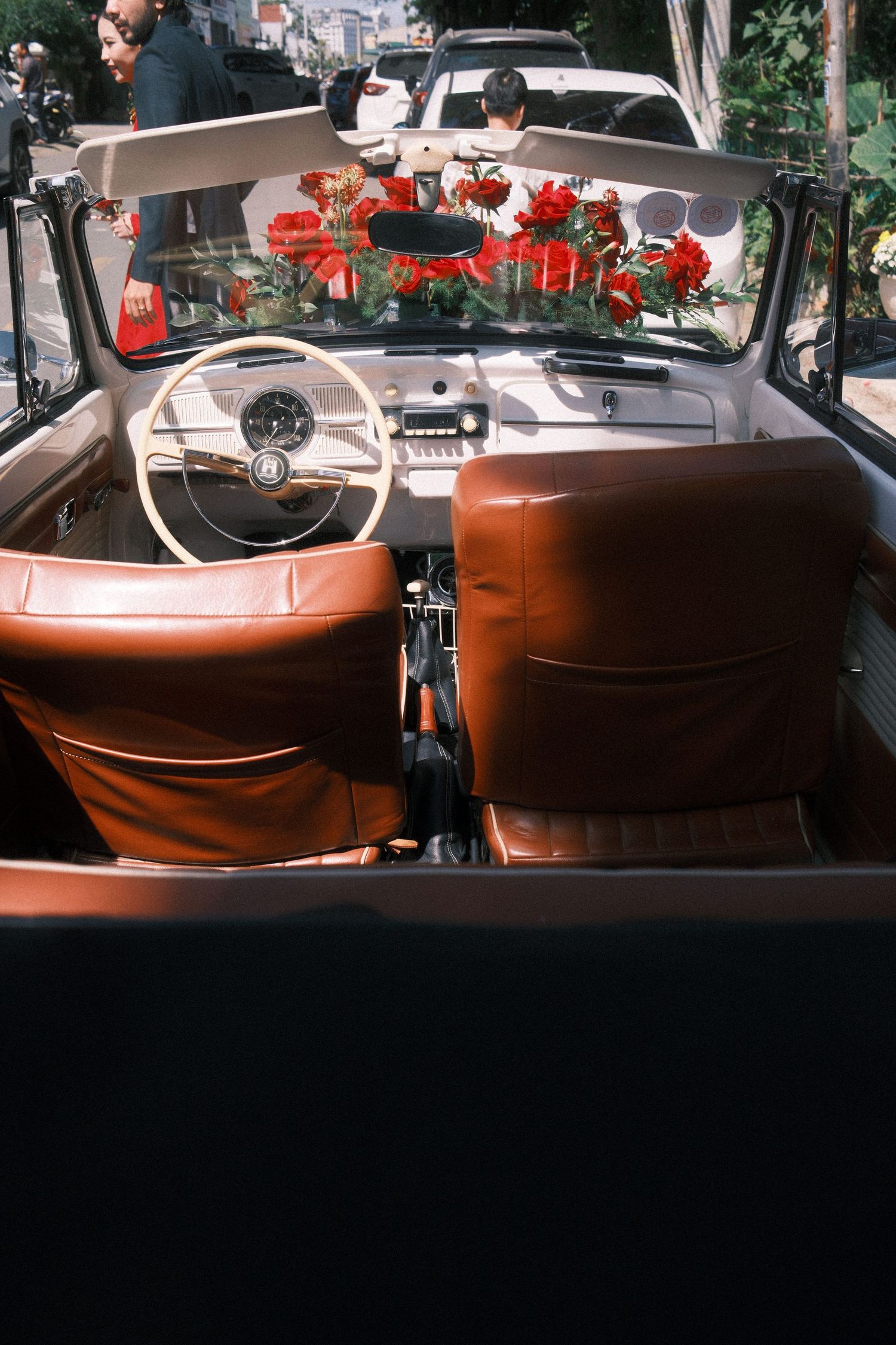 Vintage convertible car interior with brown leather seats and red roses on the dashboard.