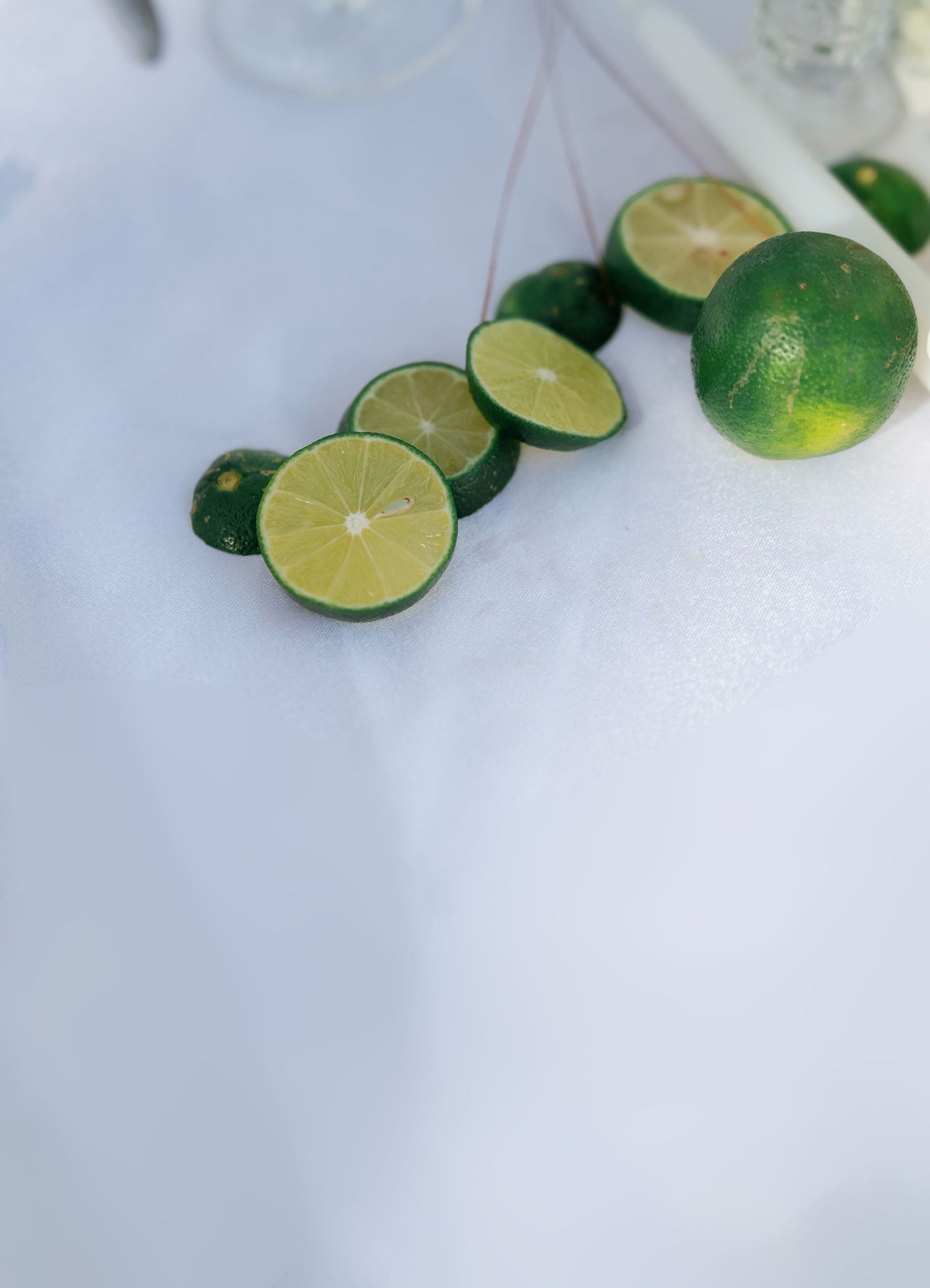 Fresh sliced green limes arranged on white surface with whole limes nearby.