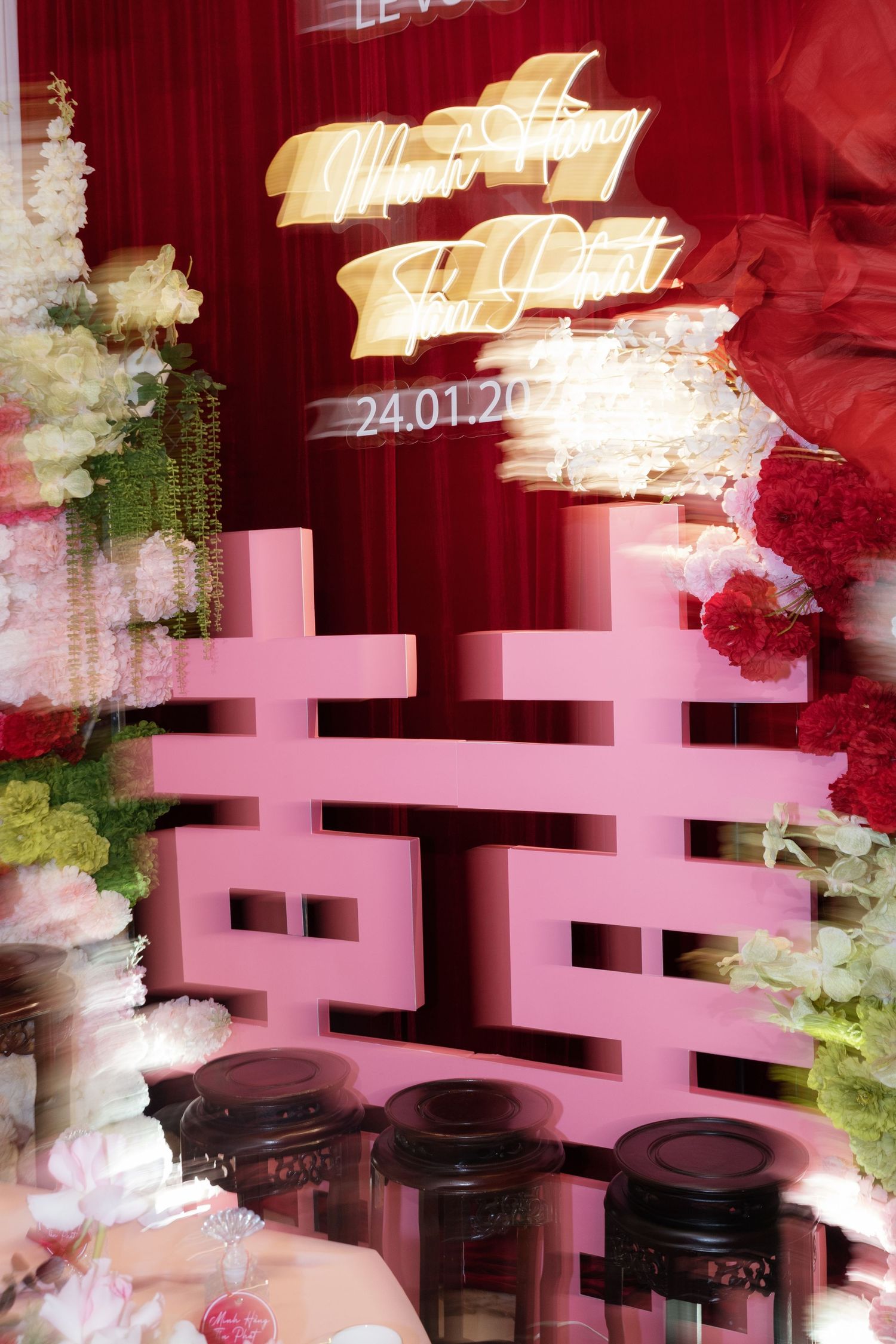 Pink double happiness symbol decorates a Chinese wedding venue with floral arrangements and golden neon signs dated 24.01.20.